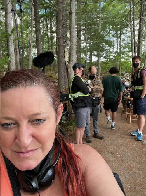 A woman taking a selfie with several people, including police officers, in a wooded outdoor area.