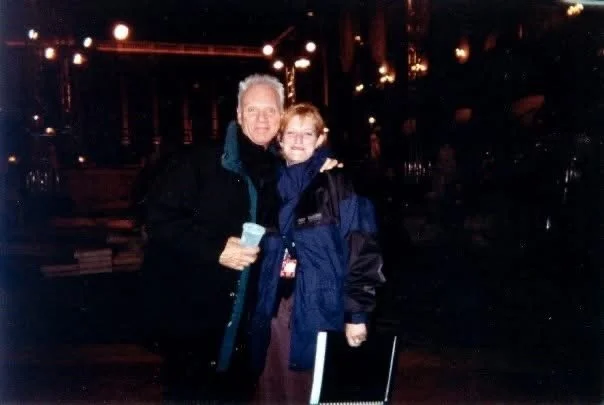 Two people, an older man and a young girl, standing close together outdoors at night, both smiling and wearing jackets.