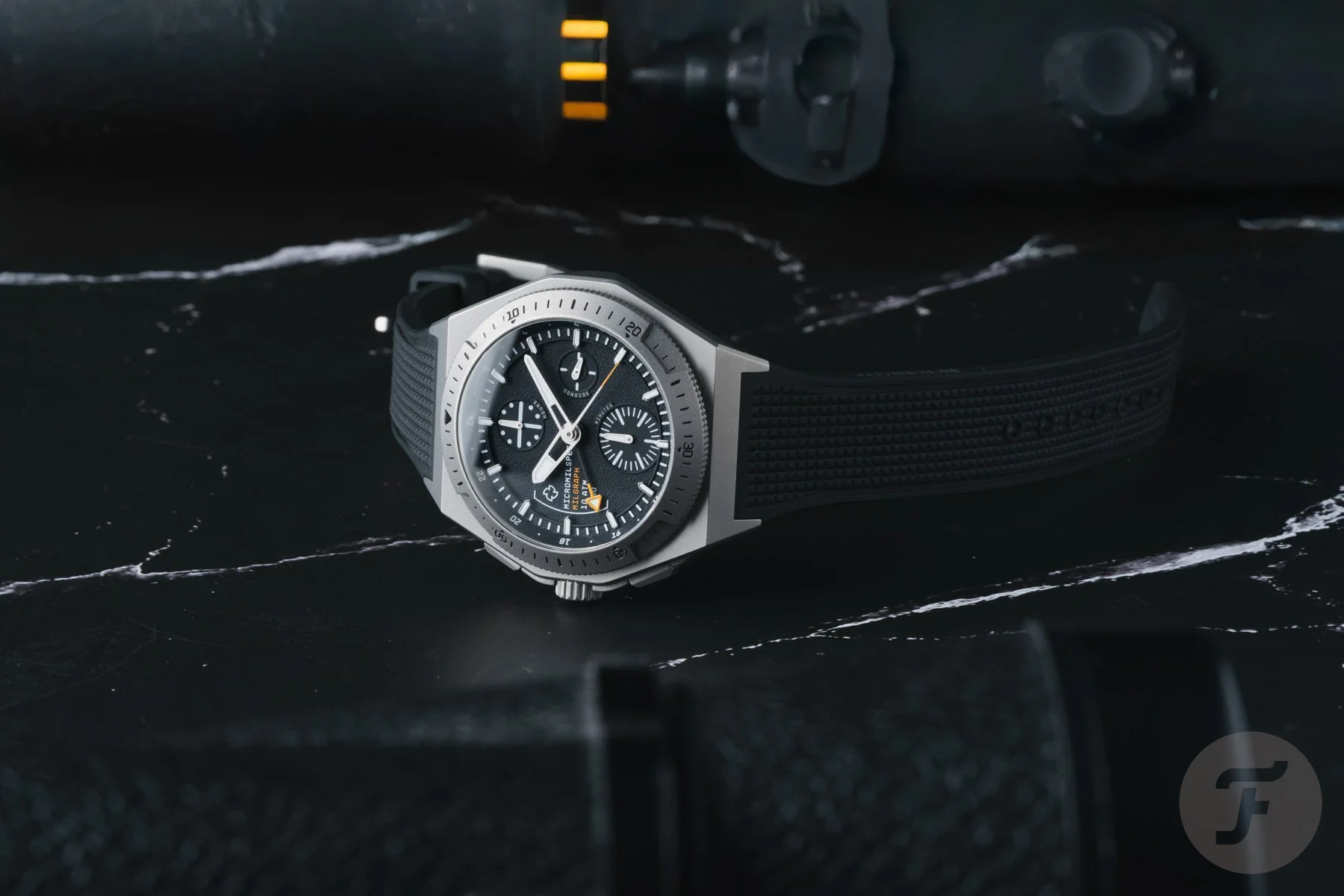 A close-up photograph of a stylish, modern wristwatch with a black face, multiple sub-dials, and a black strap, placed on a black marble surface with white veining.