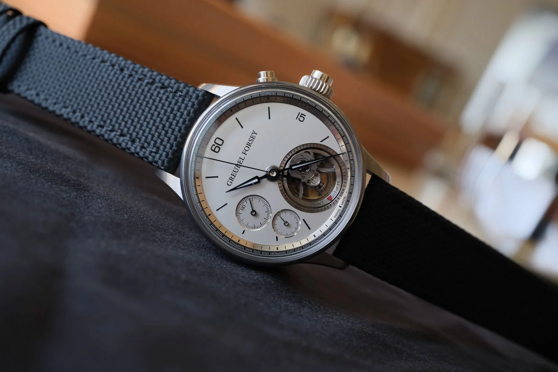 A Greubel Forsey wristwatch with a white dial, black hands, and a black strap, featuring a visible mechanical movement and additional small sub-dials.