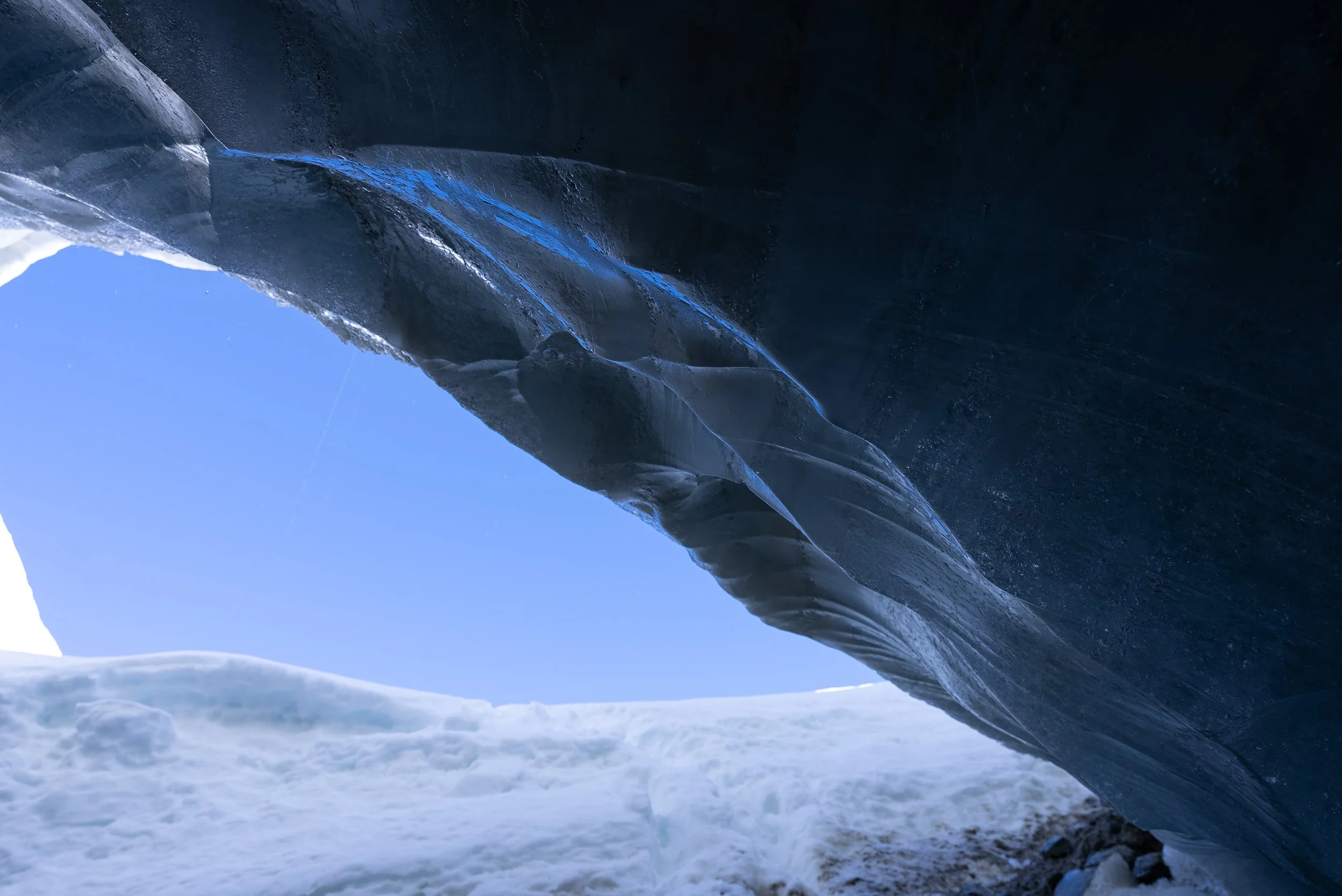 Ice cave with a large ice formation over a snowy landscape and a clear blue sky.