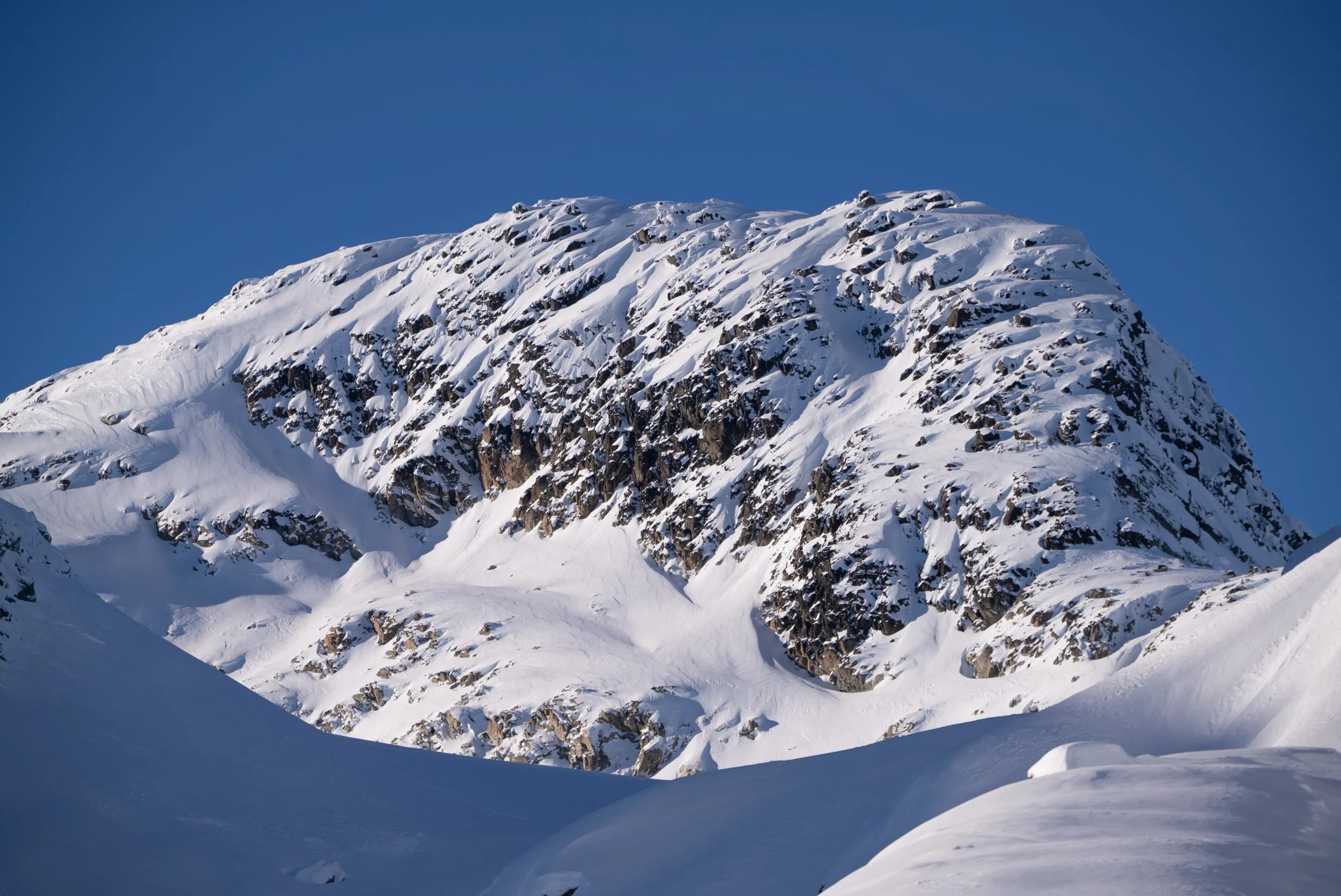 Snow-covered mountain with rocky cliffs under a clear blue sky.