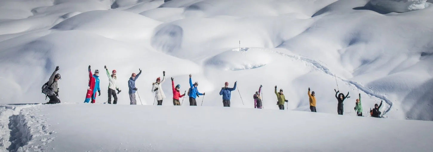 Group of people in colorful winter gear skiing or snowboarding on a snowy mountain landscape.