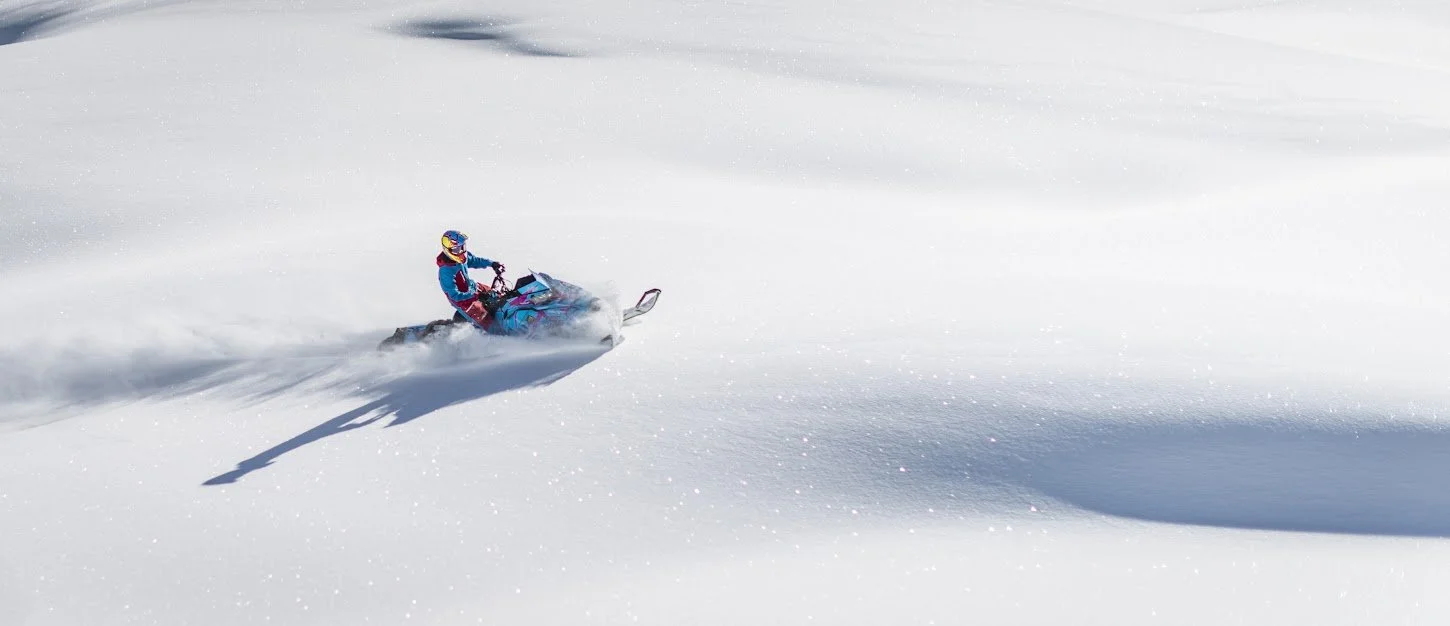 A person riding a snowmobile across a snowy landscape, leaving a trail of snow behind.