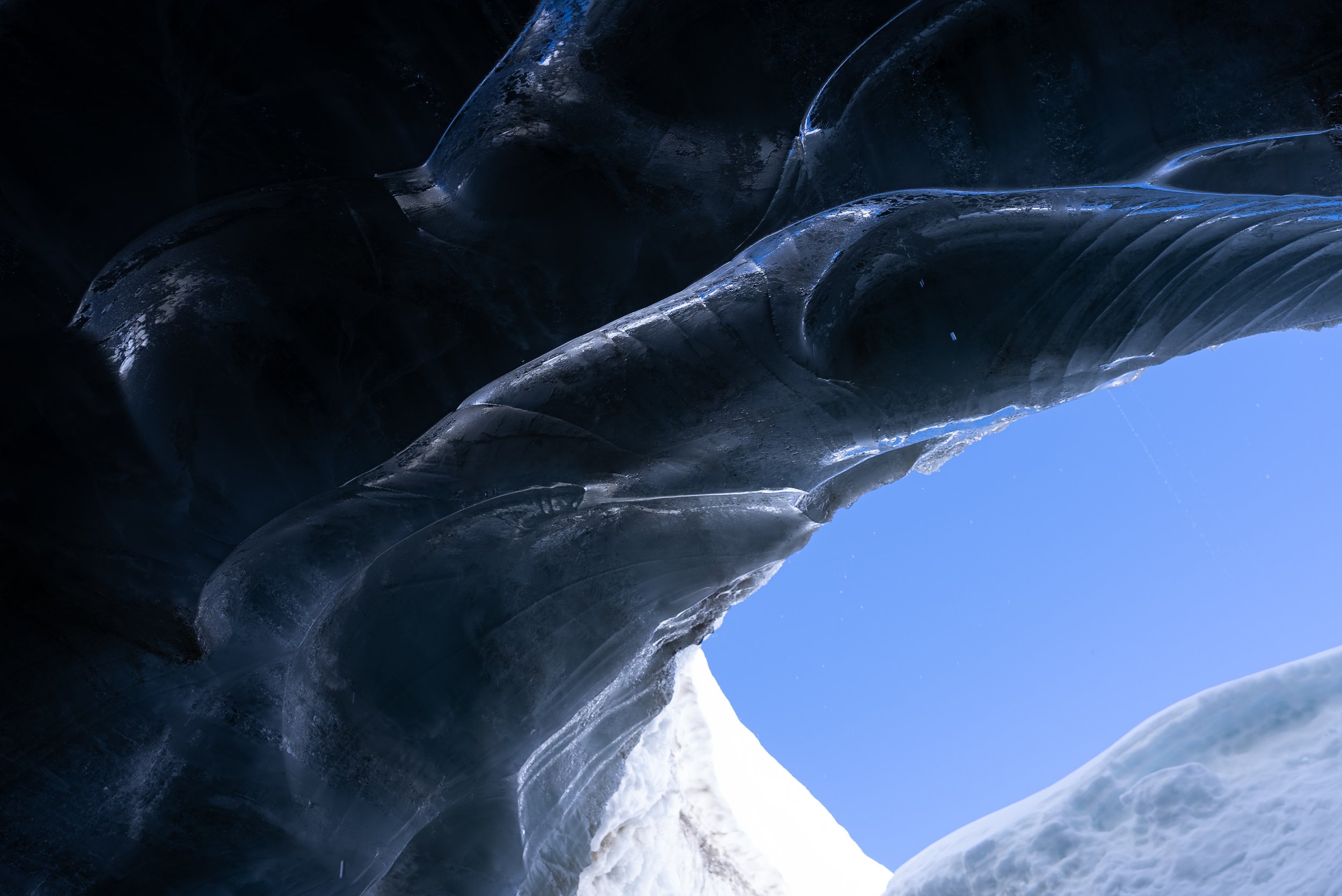 Ice cave with clear blue sky visible through an opening in the ice formation.