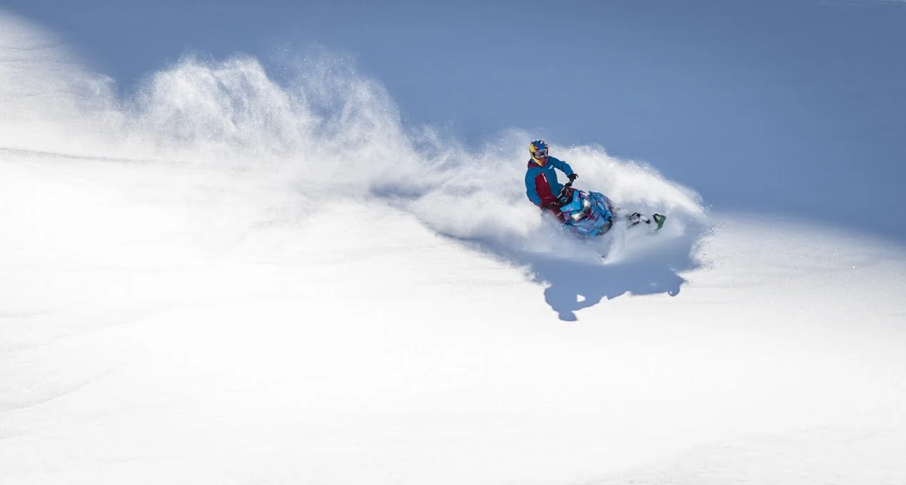 A person snowboarding down a snowy slope in bright winter gear with a helmet and goggles, creating a spray of snow.