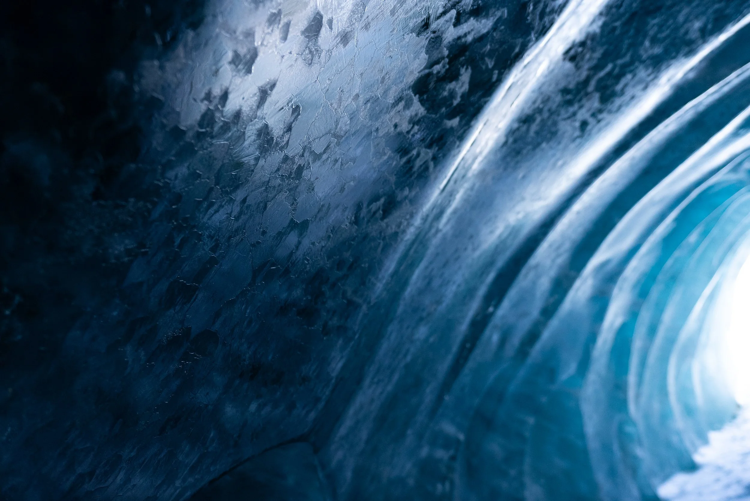 Close-up of a glacier ice tunnel with smooth, curved walls and a bright opening at the end.