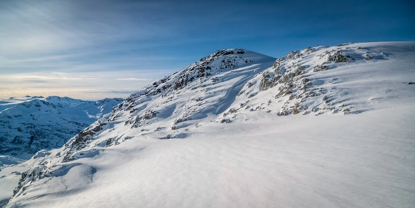 Snow-covered mountain landscape with rocky slopes and a partly cloudy sky.