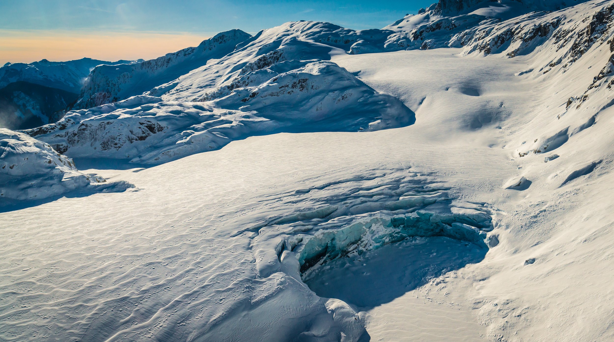 Snow-covered mountain landscape with a glacier and a crevasse in the foreground.