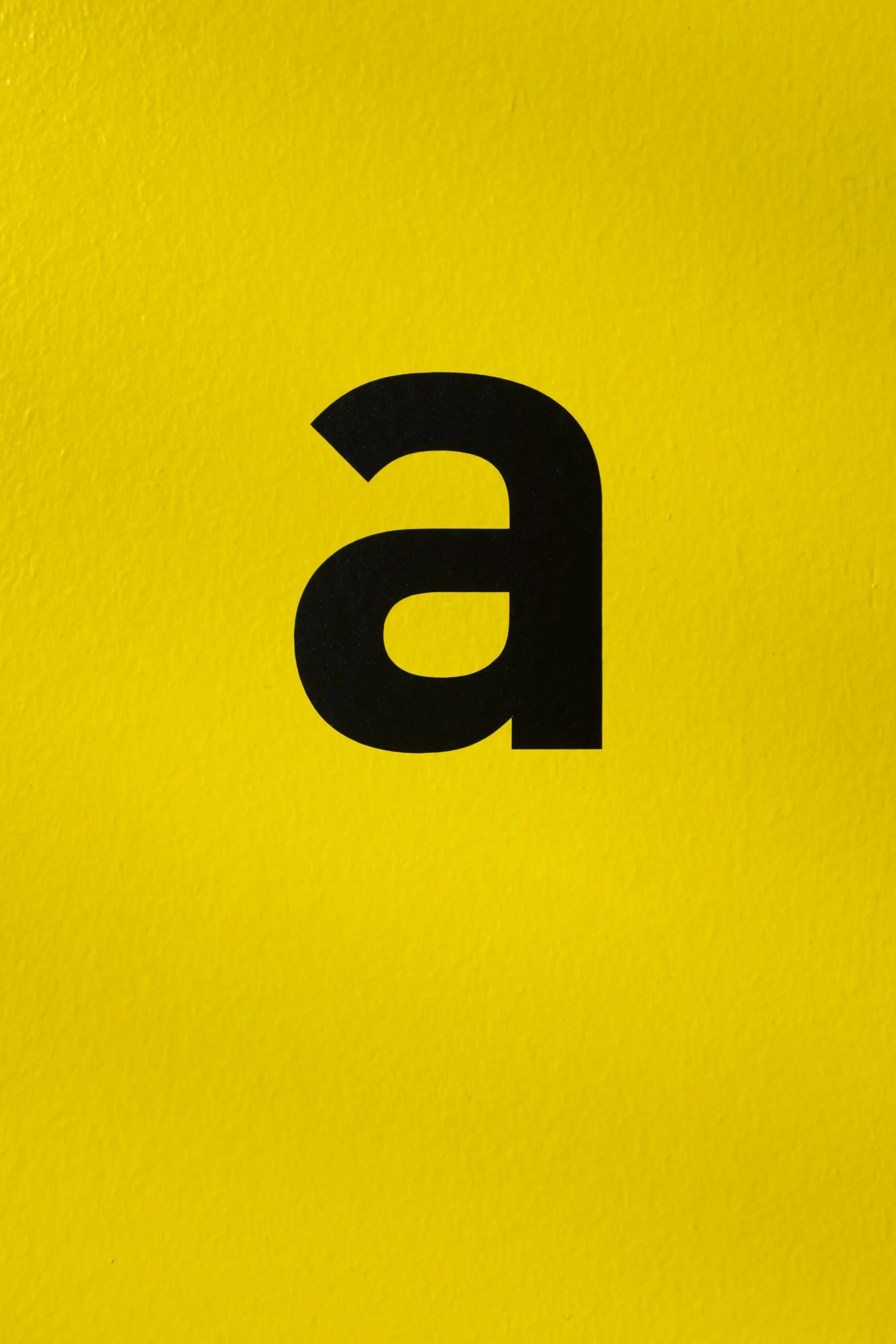 Close-up of a yellow surface with a partially visible black lowercase letter 'a'.