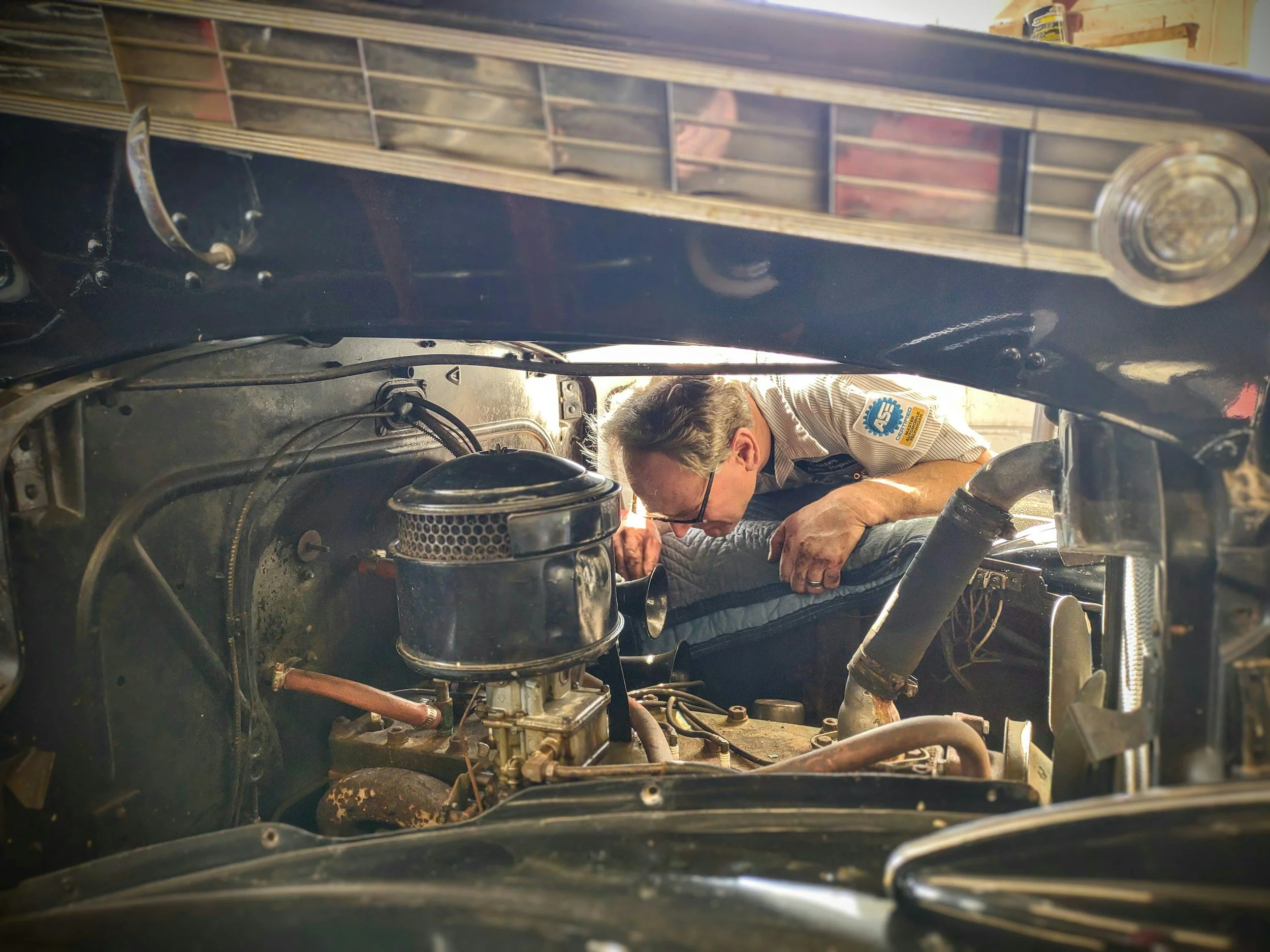 A mechanic working under the hood of a vintage car in a garage.