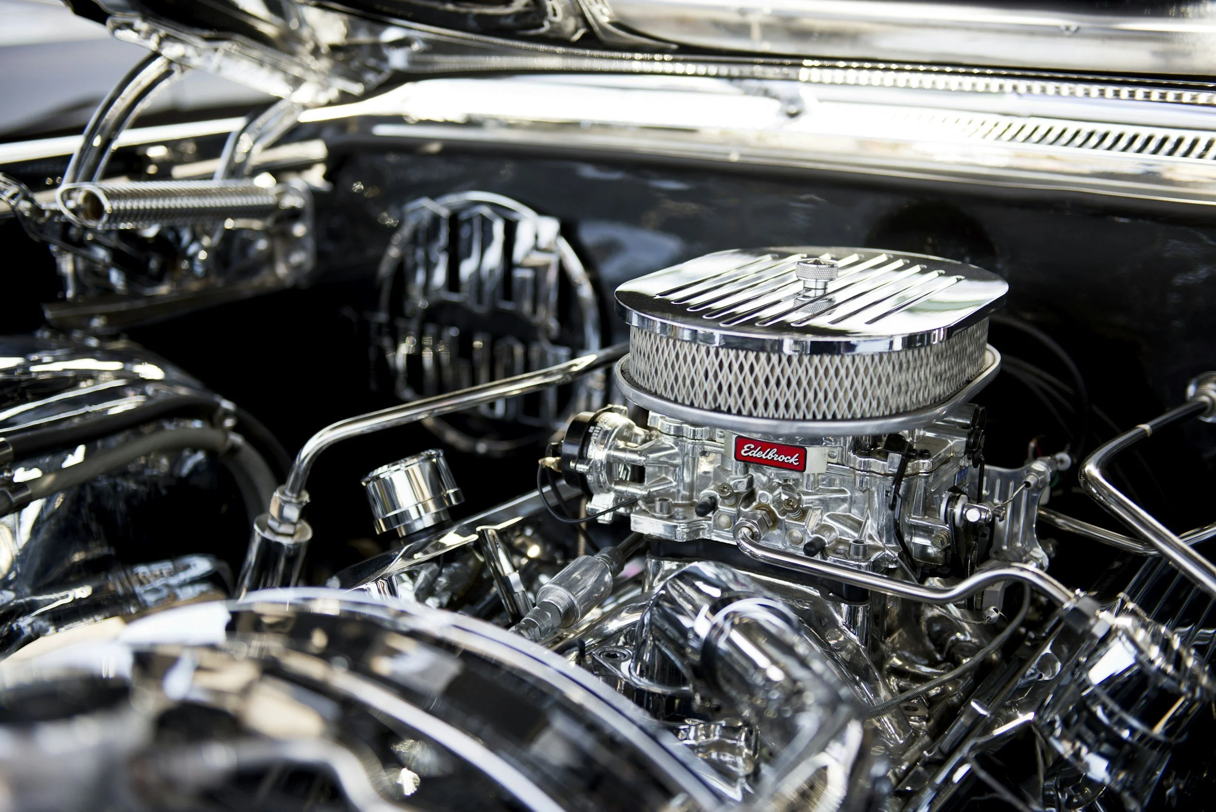 Close-up of a polished, chrome high-performance car engine with Edelbrock branding, featuring a large air filter, various metal pipes, and mechanical parts.