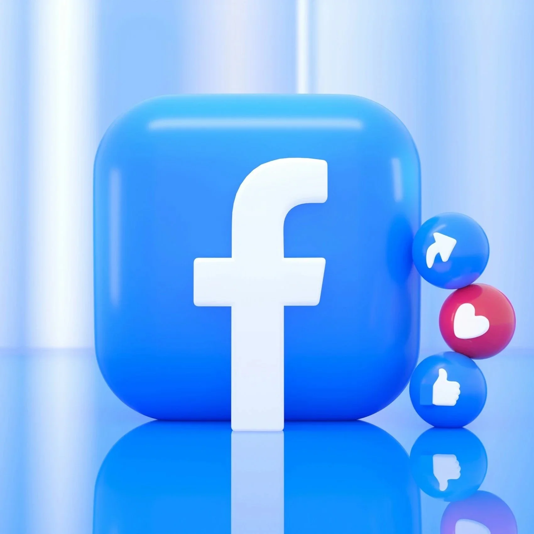 Large blue 3D Facebook logo with smaller social media reaction icons (like, love, and thumbs up) in front of a blurry digital background.