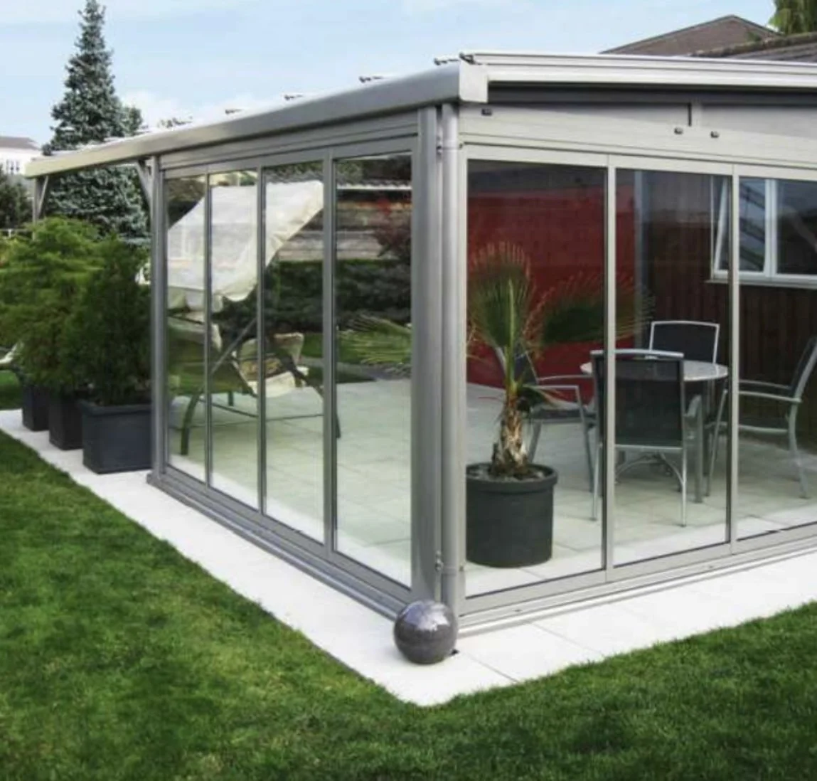 Veranda con pareti di vetro e piante, affacciata sul giardino.