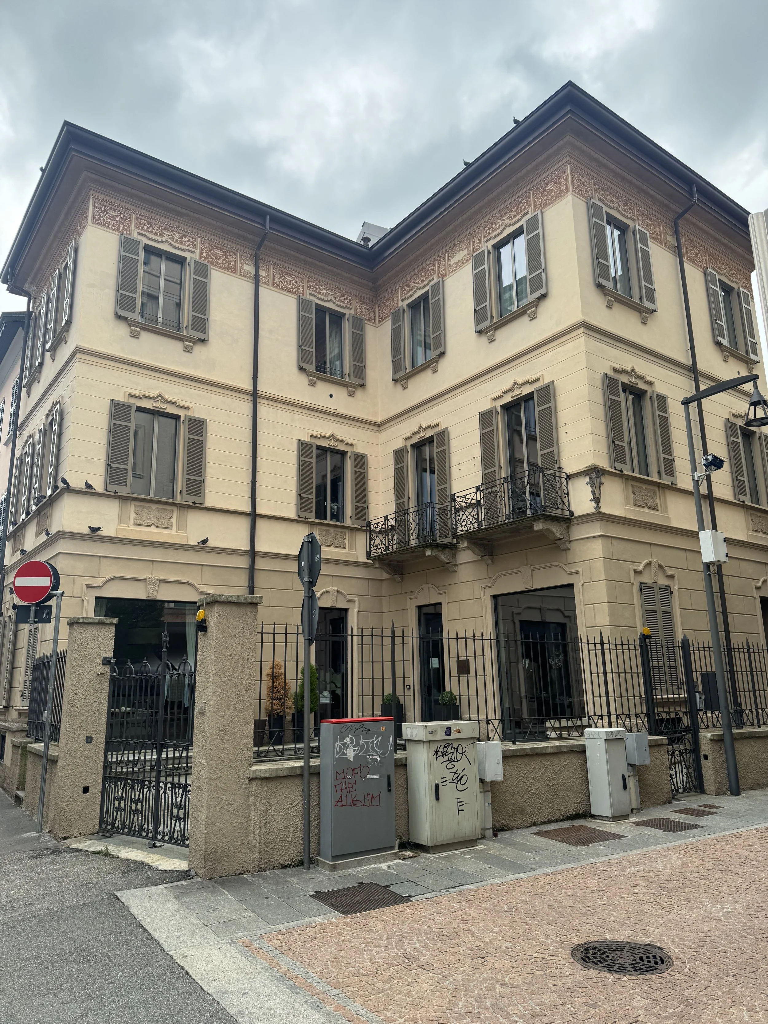 Edificio residenziale di tre piani con finestre con persiane, balcone di ferro battuto e decorazioni in stile classico, recinzione e box per lettere davanti.