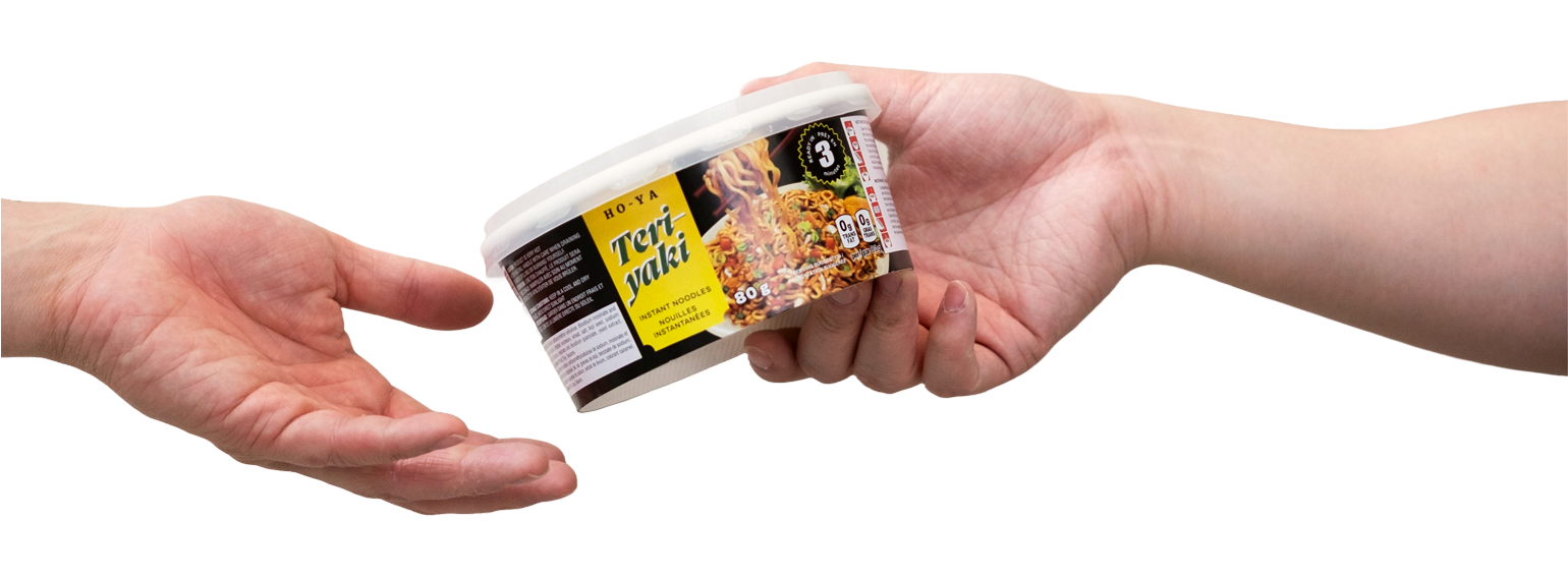 Two hands exchanging a cup of instant noodles. The cup has a black, yellow, and white label with an image of noodles and the text 'HO-YA Teri Yak'.