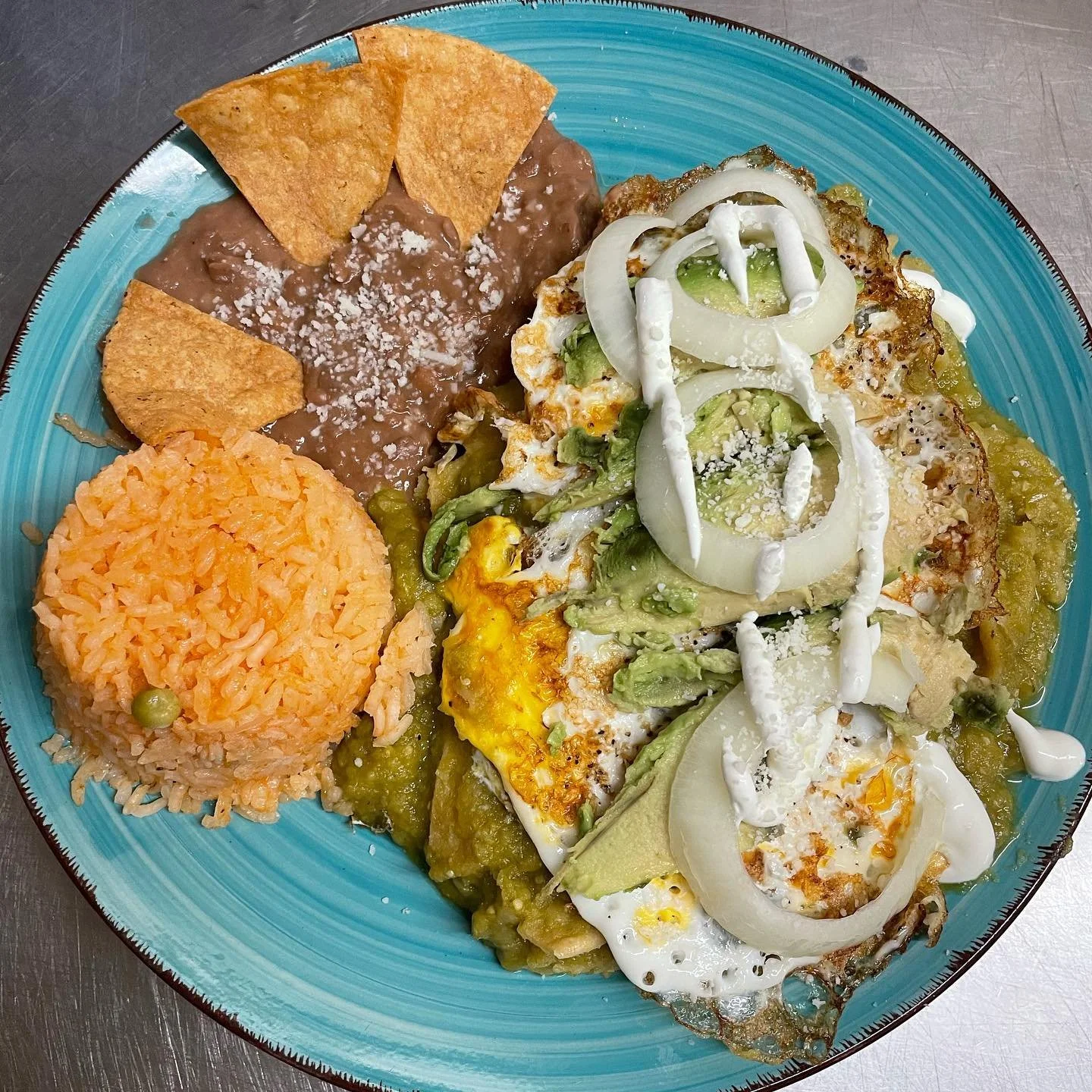 Plate of Mexican food with rice, beans with cheese, and savory scrambled eggs topped with onion, green chili, and cream.