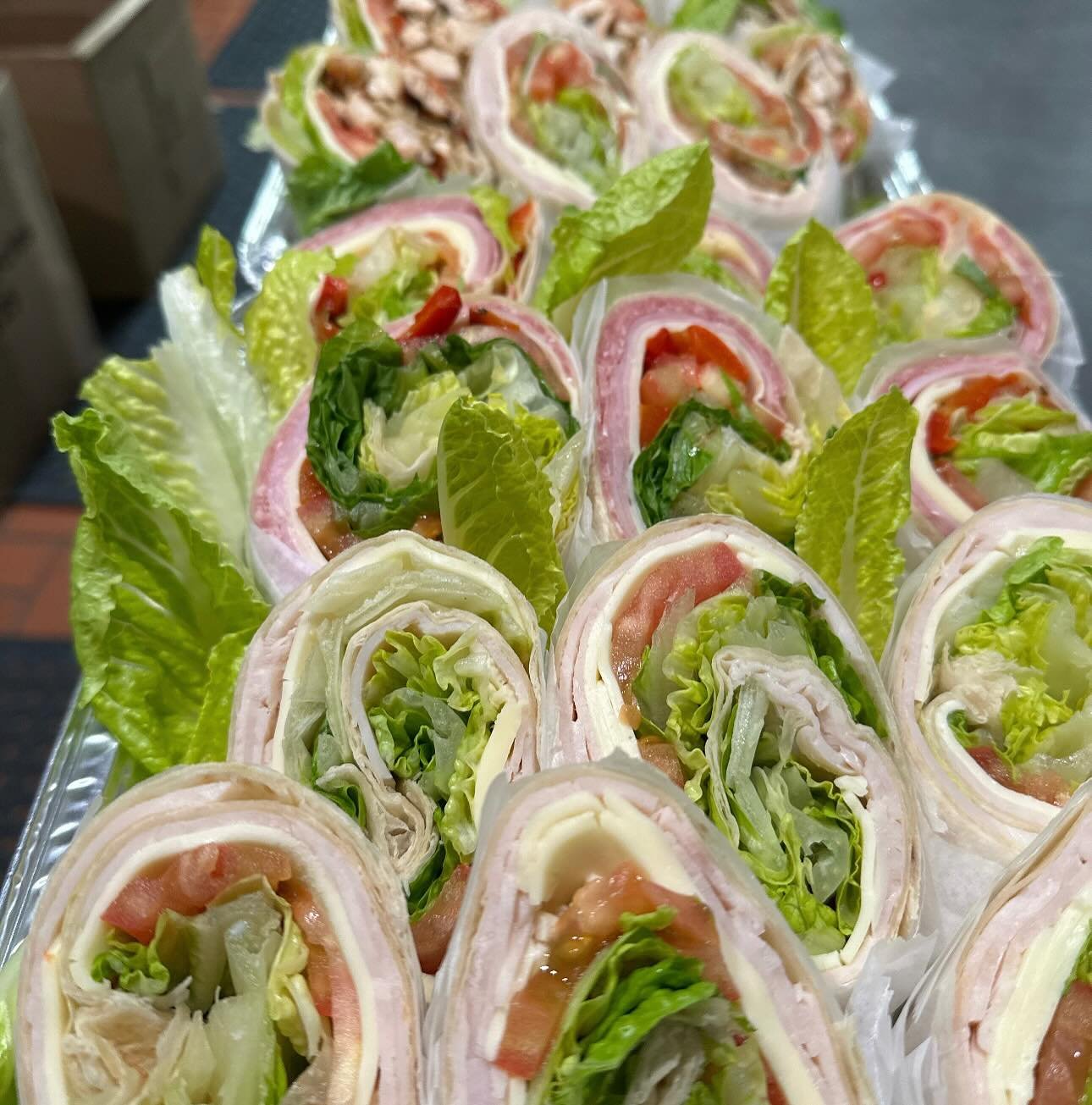 A tray of freshly prepared deli egg and lettuce wraps with turkey, cheese, tomato, and leafy green vegetables.