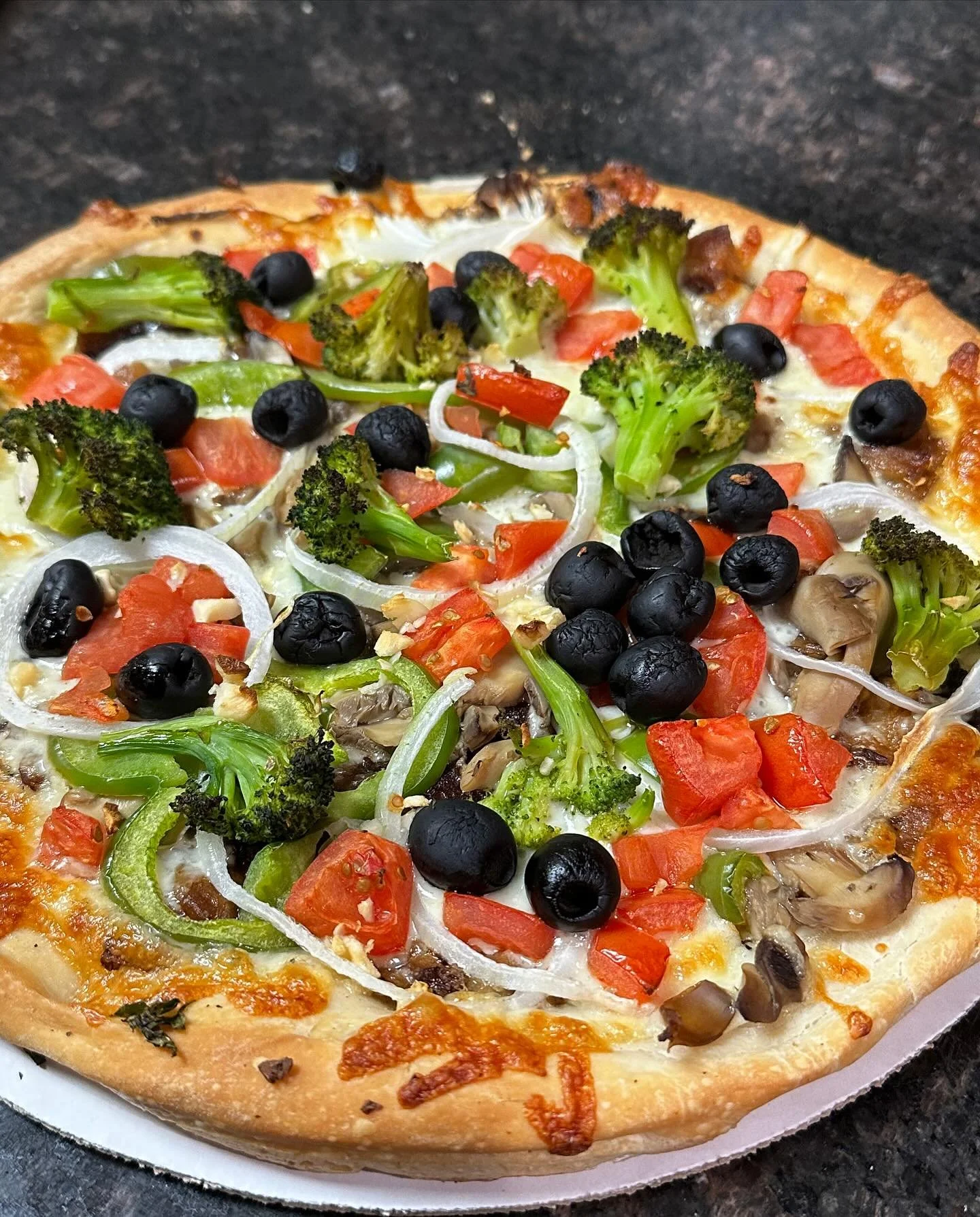 Close-up of a vegetable pizza with broccoli, black olives, tomatoes, onions, mushrooms, and green peppers.