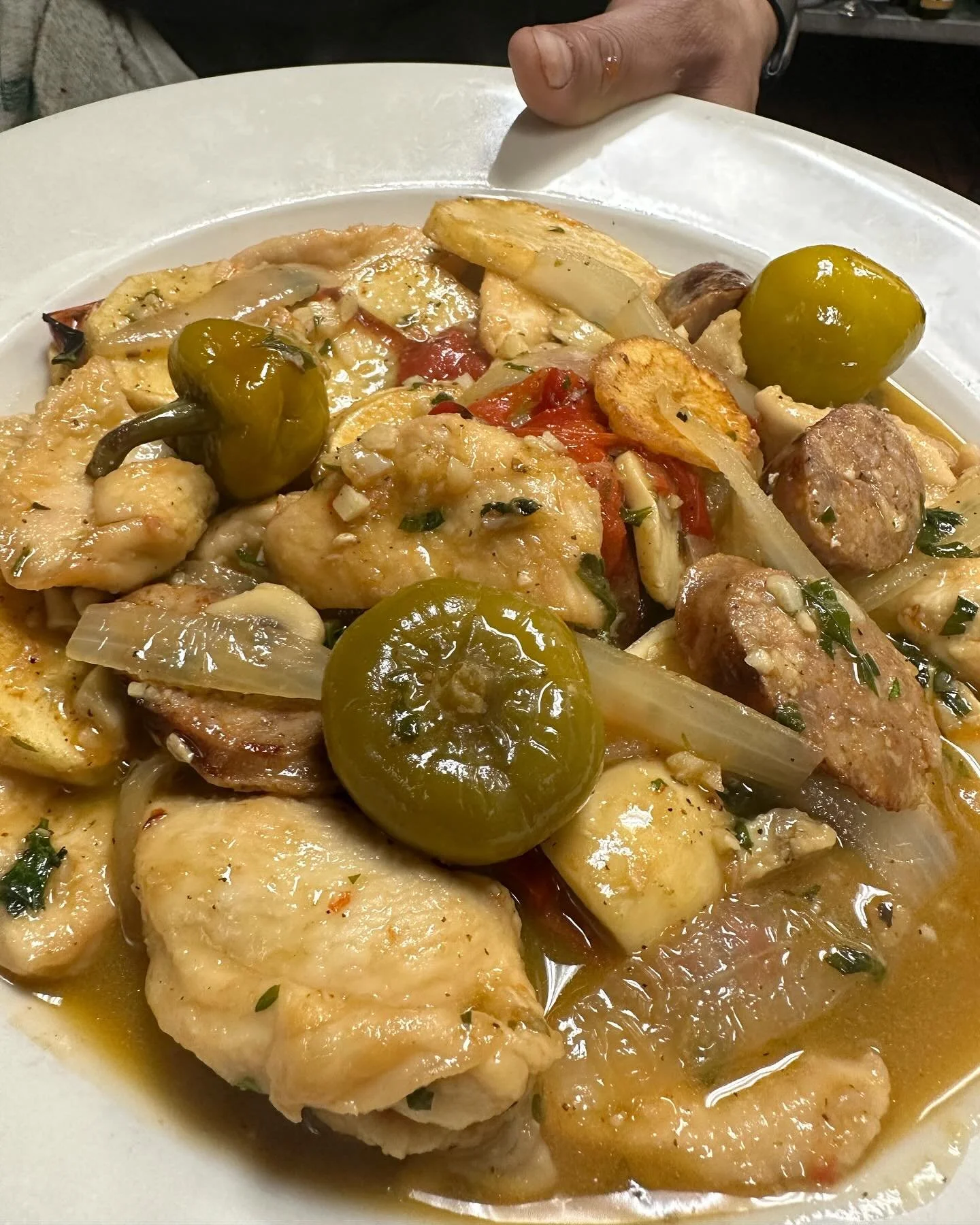 A plate of chicken, sausage, potatoes, onions, green peppers, and pickles in a savory sauce.