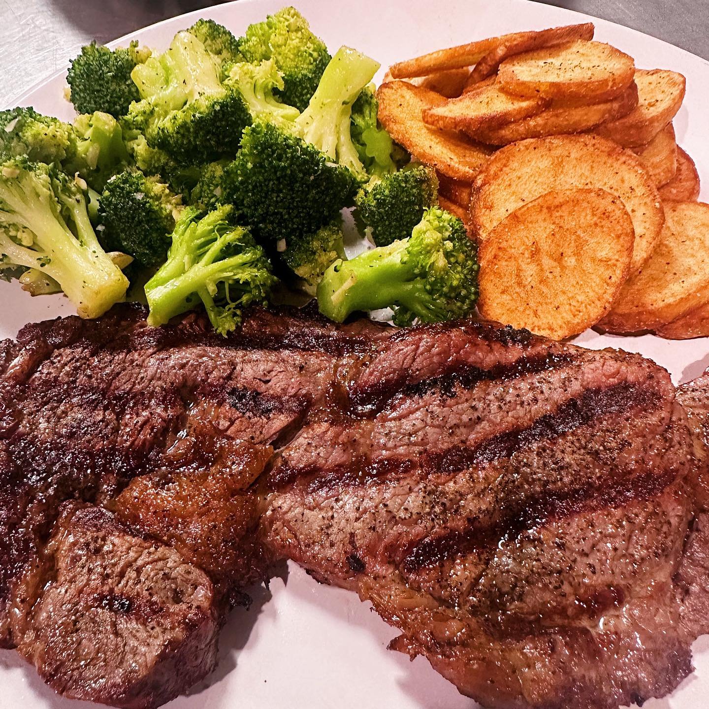 A plate of food with grilled steak, broccoli, and potato chips.