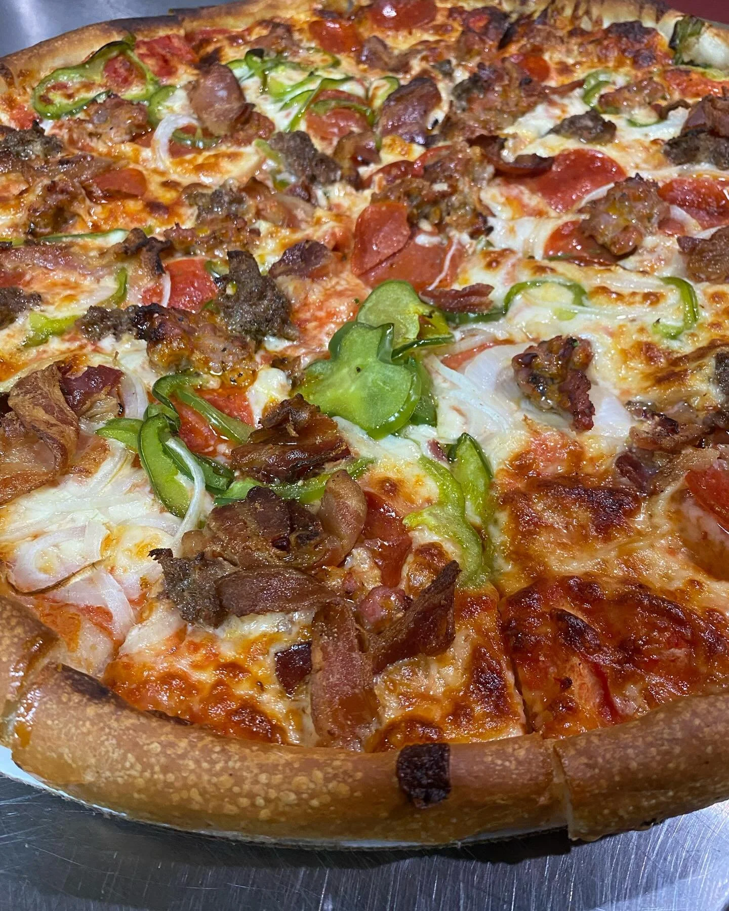 Close-up of a pizza topped with green bell peppers, bacon, onions, and pepperoni.