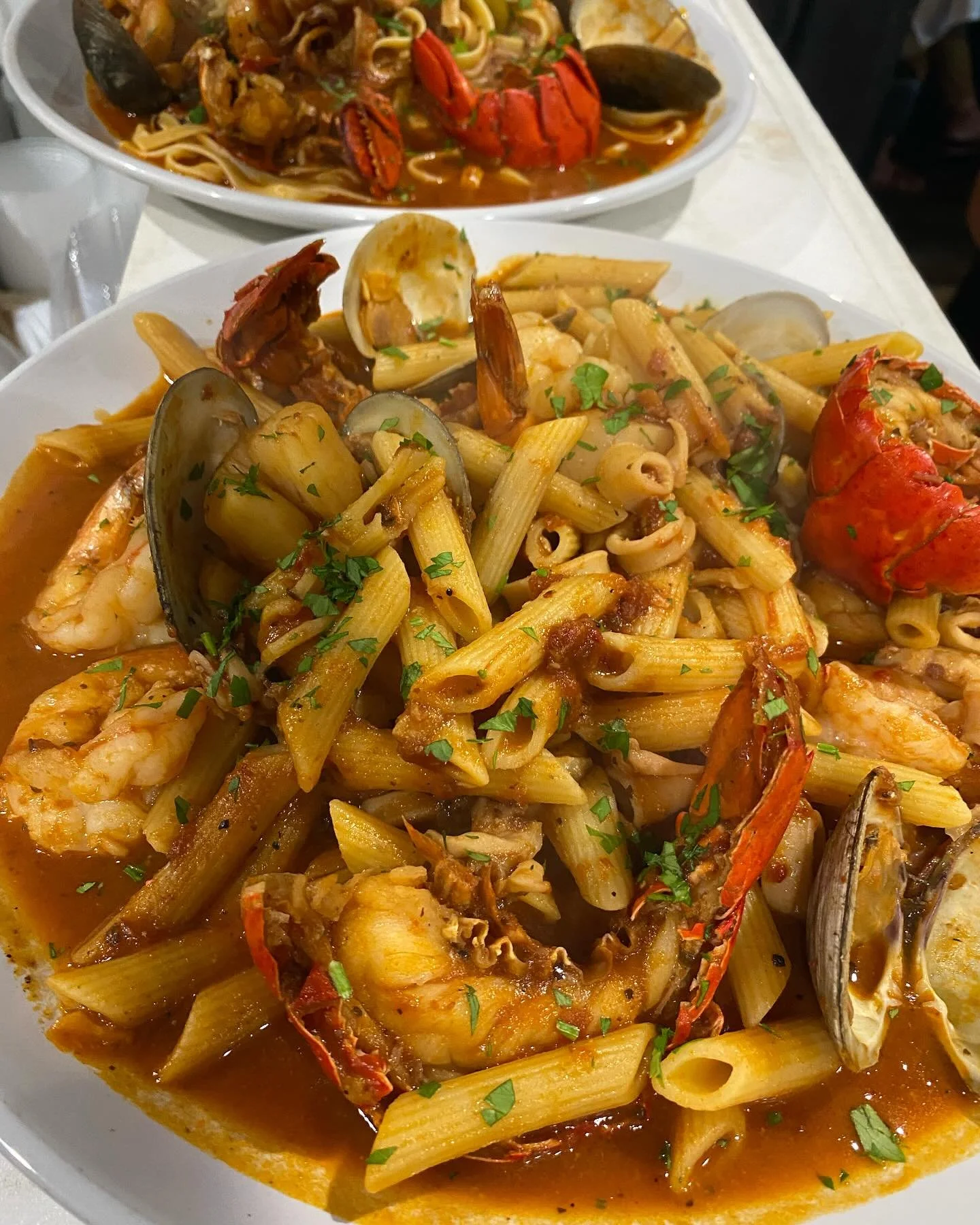 Seafood pasta with shrimp, lobster, clams, penne, and vegetables in a tomato-based sauce garnished with chopped parsley