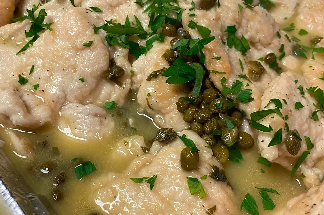 Cooked chicken thighs garnished with chopped parsley and green peppercorns in a light sauce or broth.