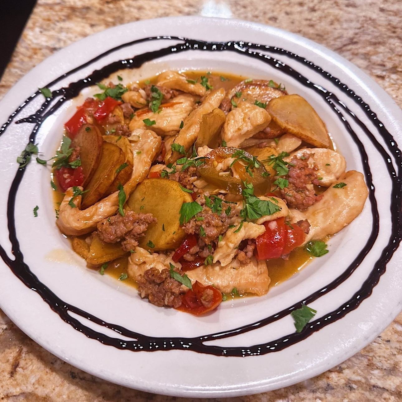 Plate of seasoned stir-fried chicken, ground beef, potatoes, tomatoes, and herbs garnished with chopped cilantro, with a decorative black sauce drizzle on the white plate.