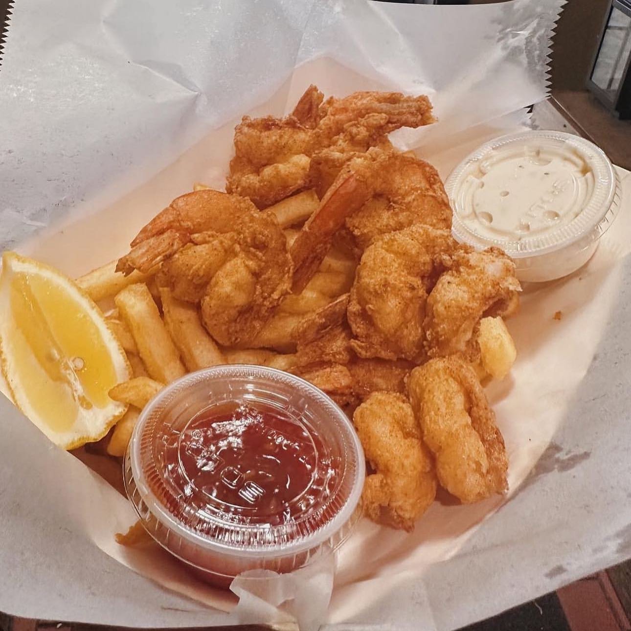 Basket of fried chicken wings, French fries, two lemon wedges, and dipping sauces (ketchup and ranch dressing) on a paper-lined tray.