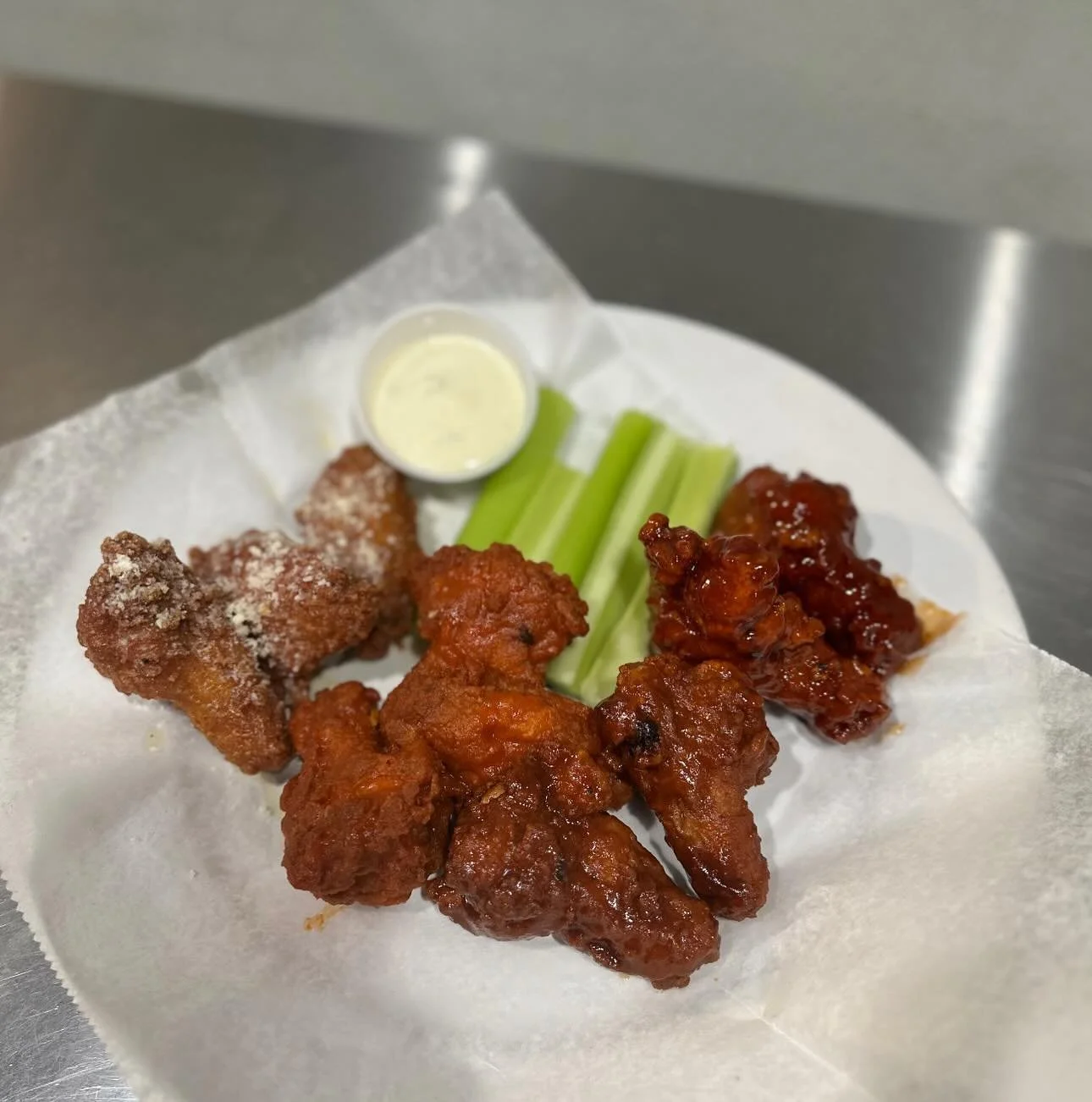 Plate of fried chicken with sauce, celery sticks, a small cup of dipping sauce, and a piece of breaded chicken