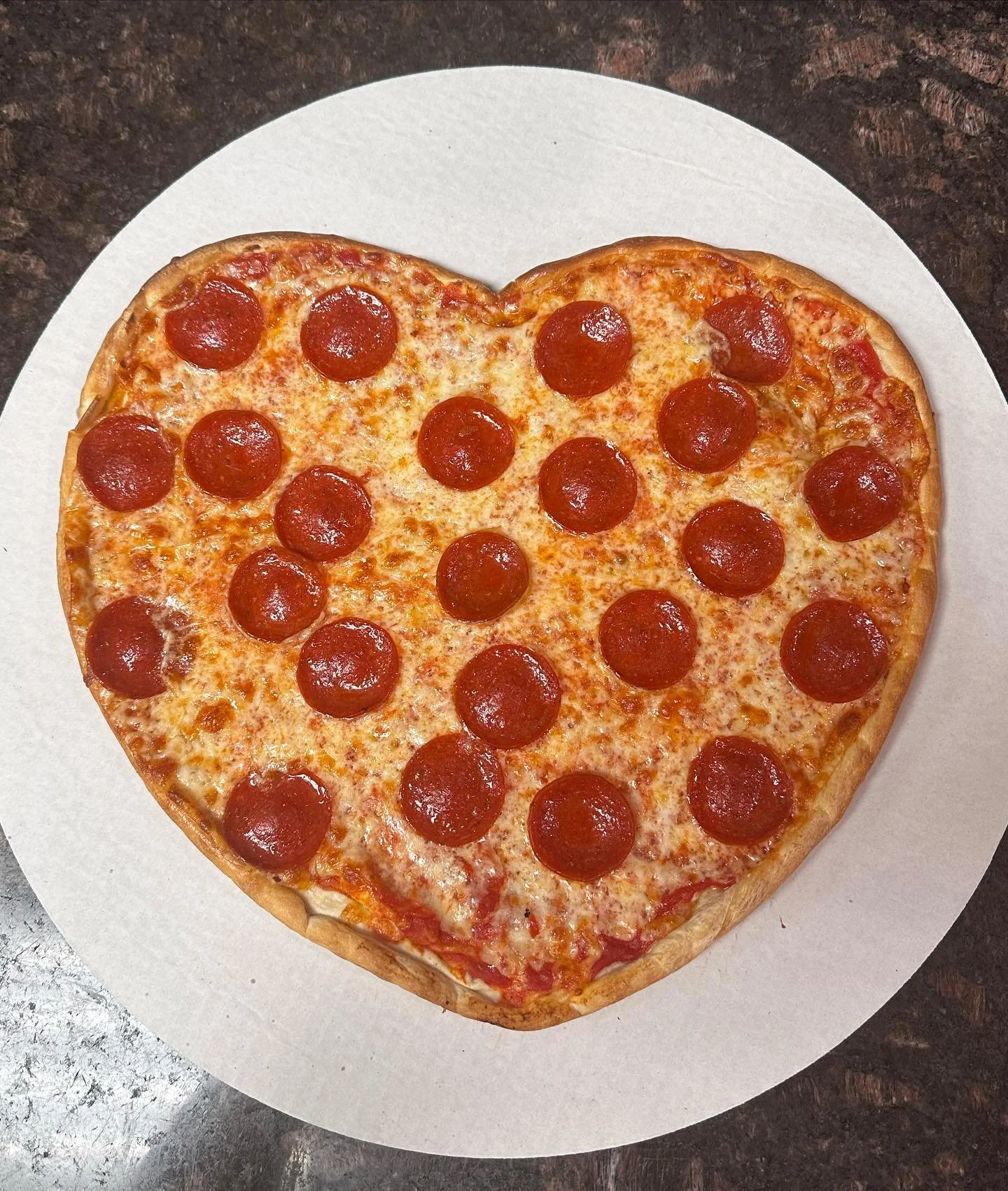 Heart-shaped pepperoni pizza on a white plate.