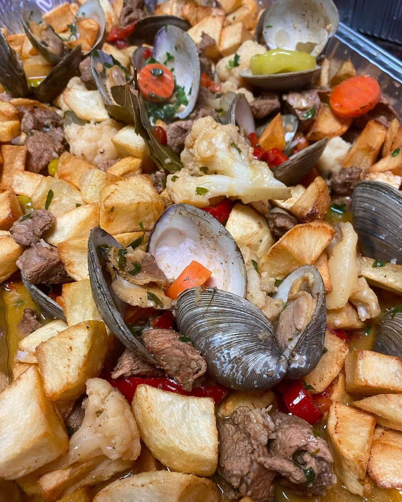 Close-up of a seafood boil with cooked clams, potatoes, beef, cauliflower, red bell peppers, and onion.