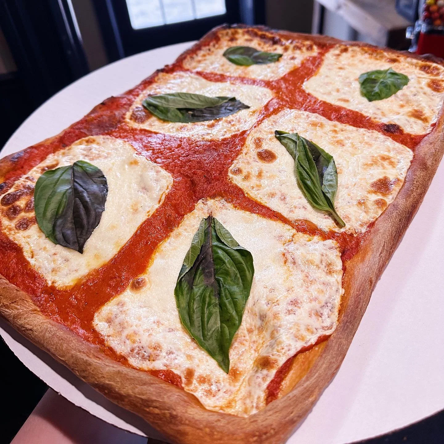 Rectangular pizza with four cheese slices topped with fresh basil leaves.
