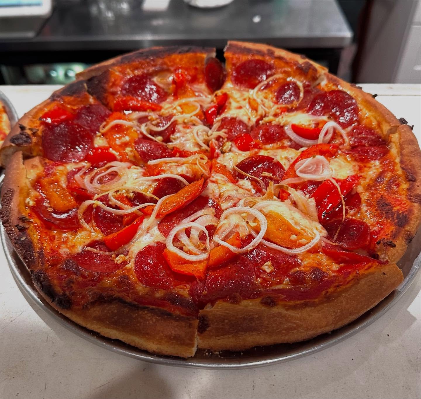A pepperoni pizza with red and yellow bell peppers and onions on a metal pizza tray.