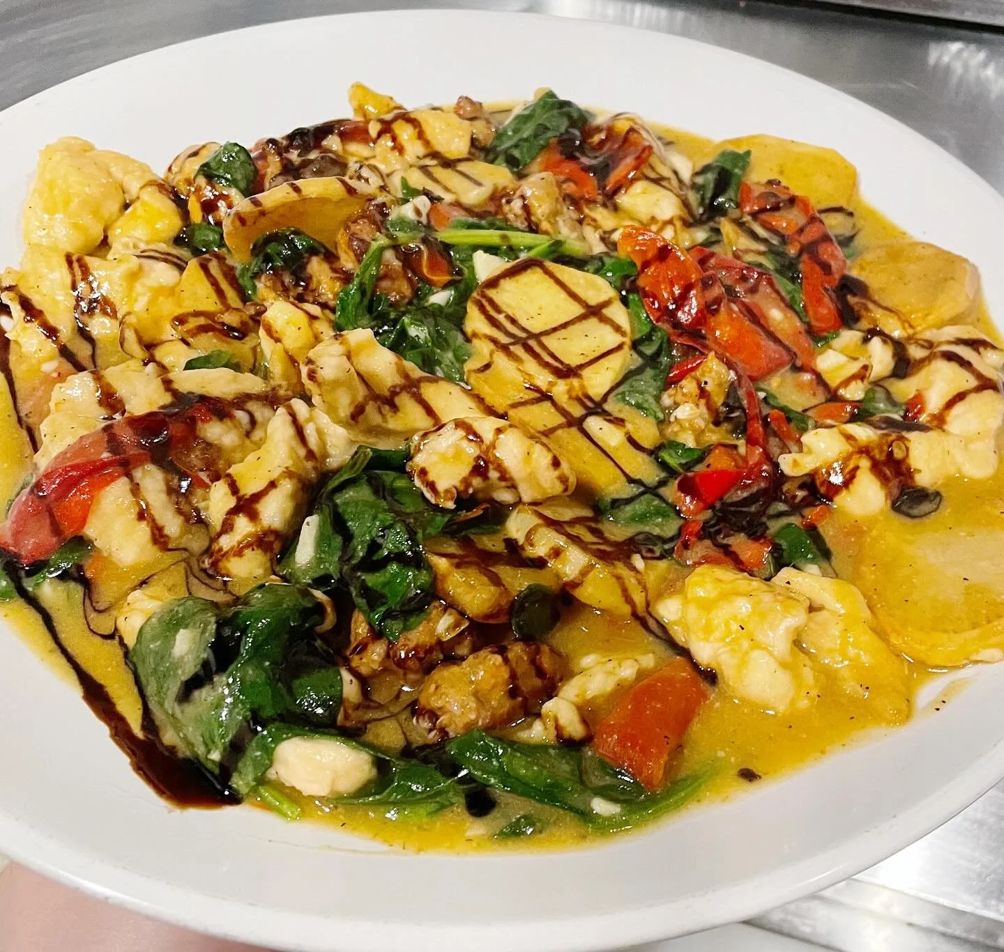 A plate of stir-fried vegetables with chicken, drizzled with dark sauce and topped with sliced banana, with a yellow sauce underneath.