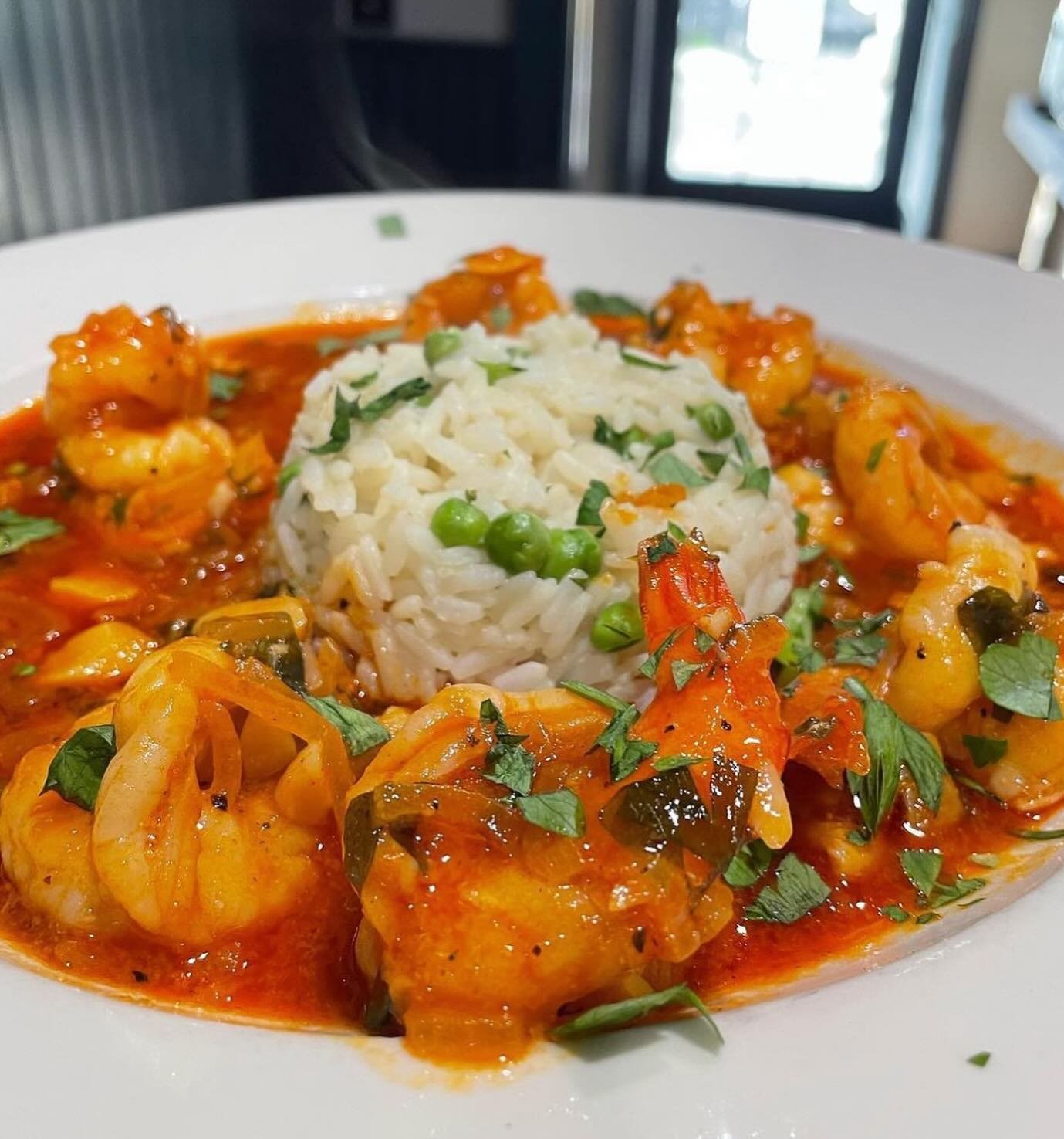 Shrimp curry with rice and green peas garnished with chopped herbs on a white plate