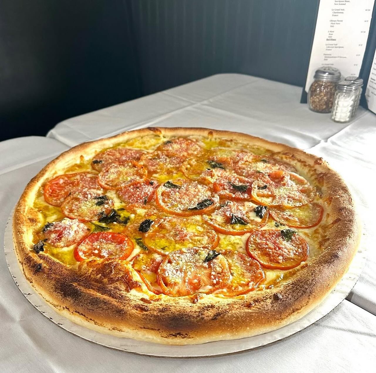 A freshly baked pizza on a white tablecloth, topped with tomato slices, melted cheese, and black olives.