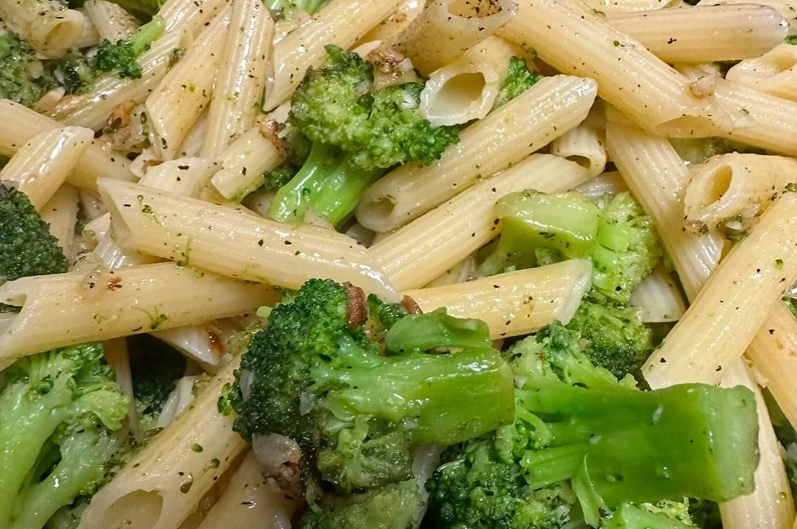 Close-up of cooked penne pasta with broccoli and green vegetables, seasoned with herbs and spices.