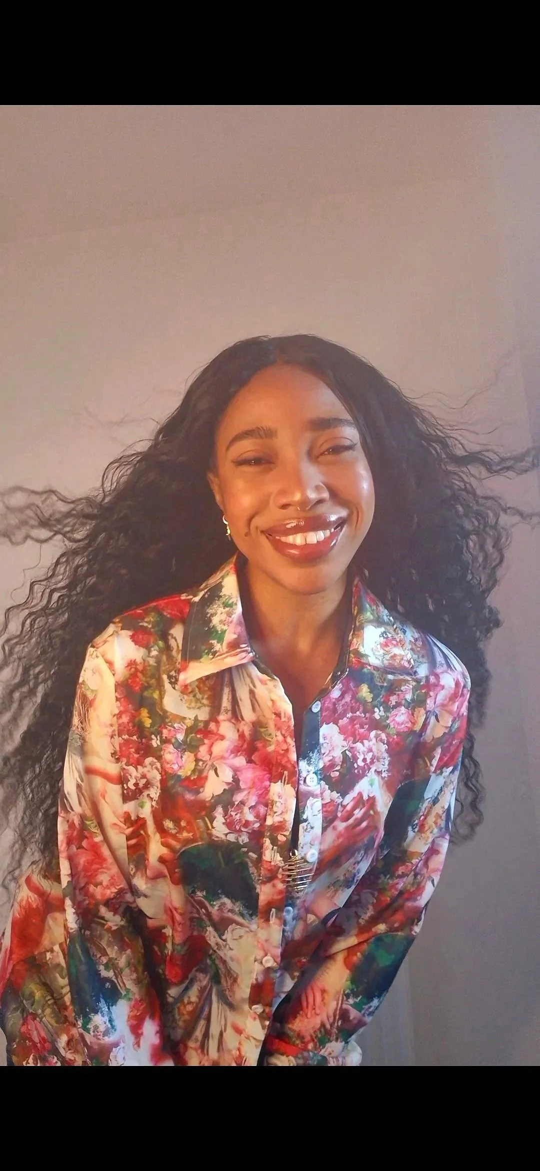 Kiara Zhanae with curly black hair smiling, wearing a colourful floral button-up shirt.