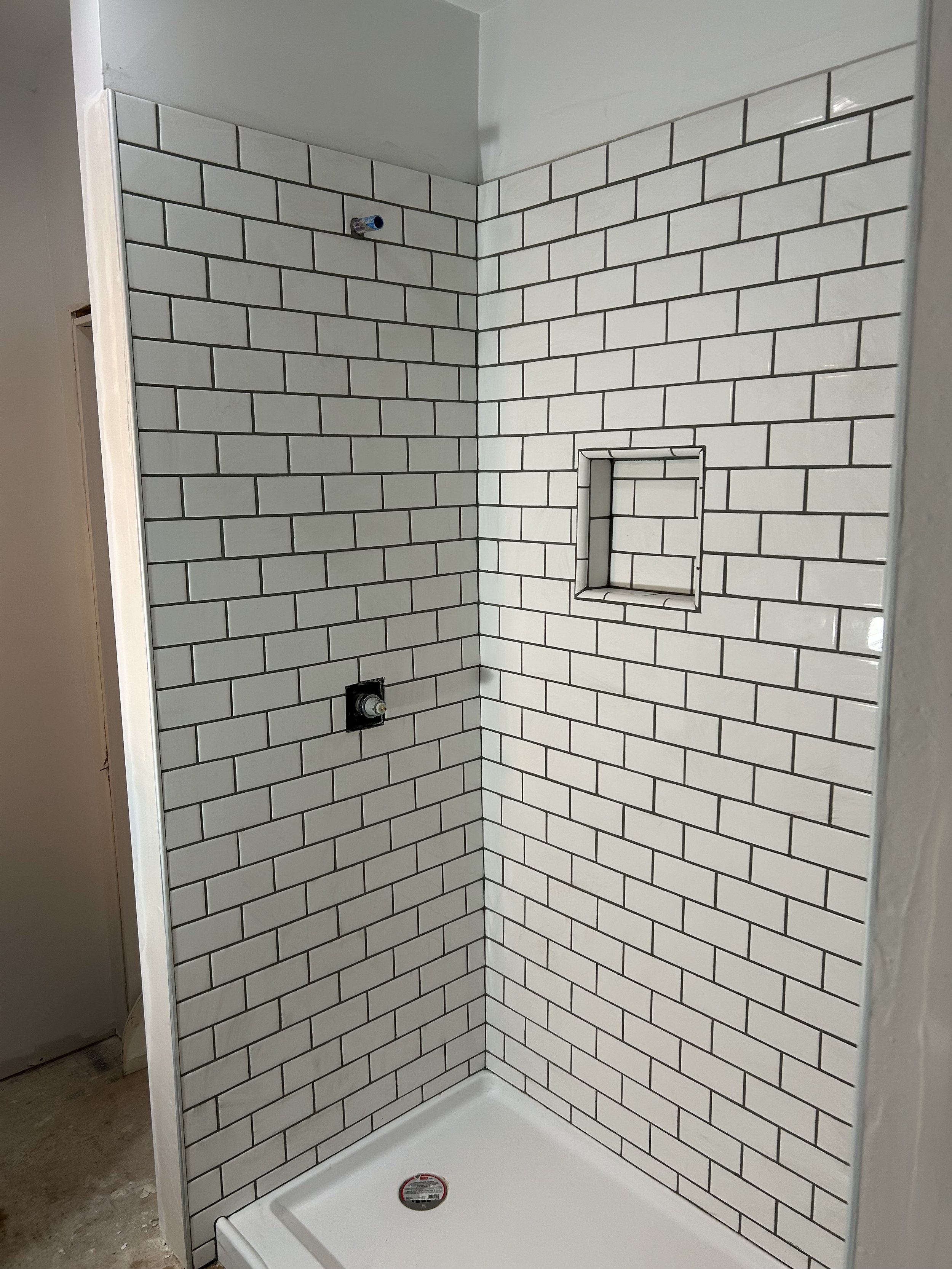 Newly built walk-in shower with white subway tiles, a built-in niche, and a shower tray, awaiting fixtures and finishing touches.