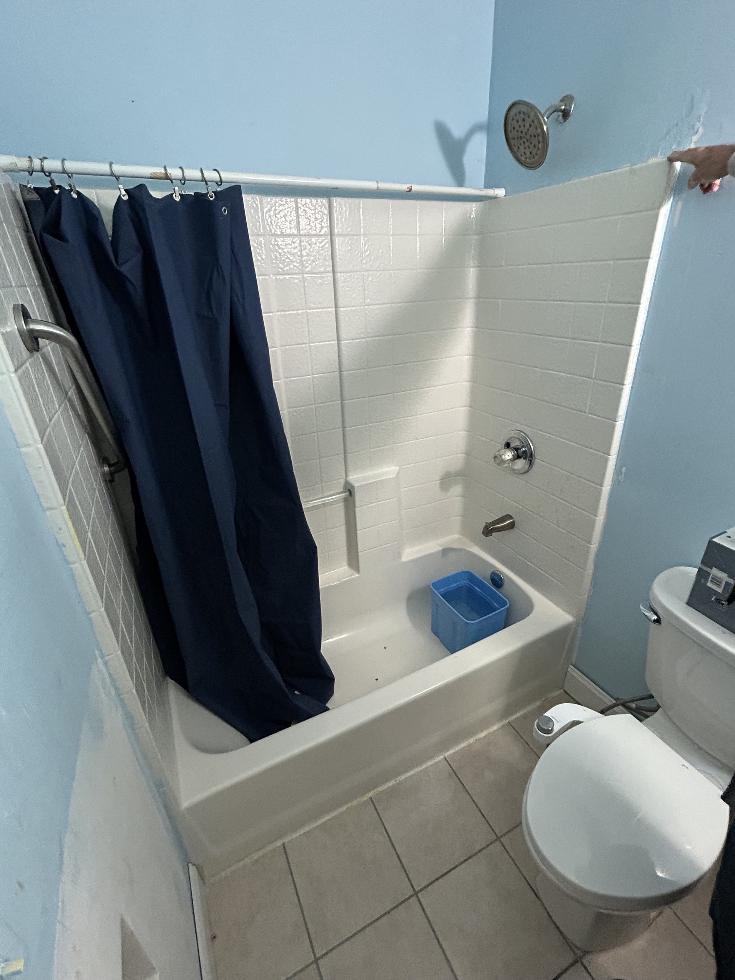 Small bathroom with a bathtub, blue shower curtain, showerhead, and toilet. Blue plastic bin in the bathtub, and light blue painted walls.