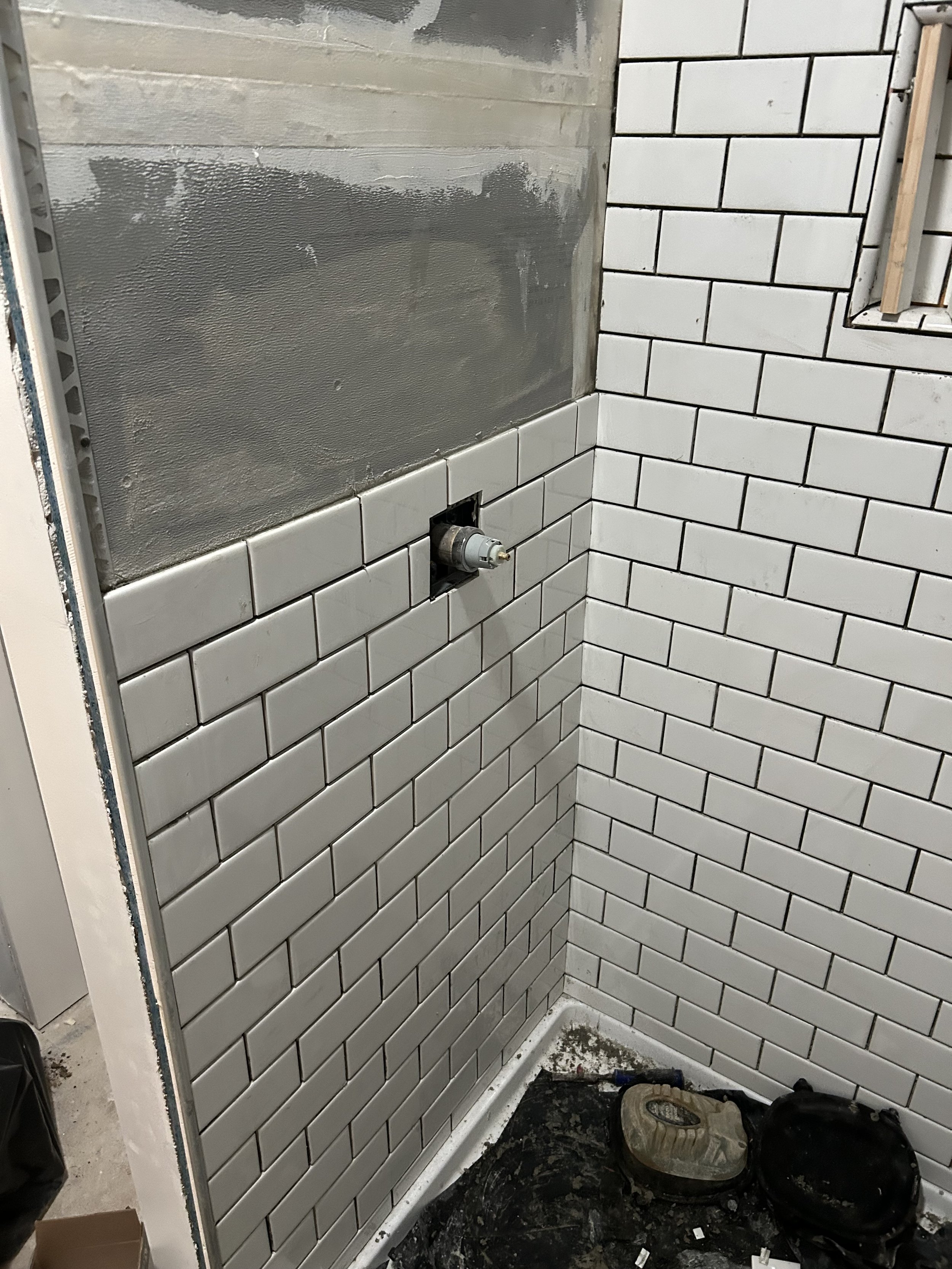 Partially tiled bathroom wall with white subway tiles, an electrical box, and construction tools on the floor.