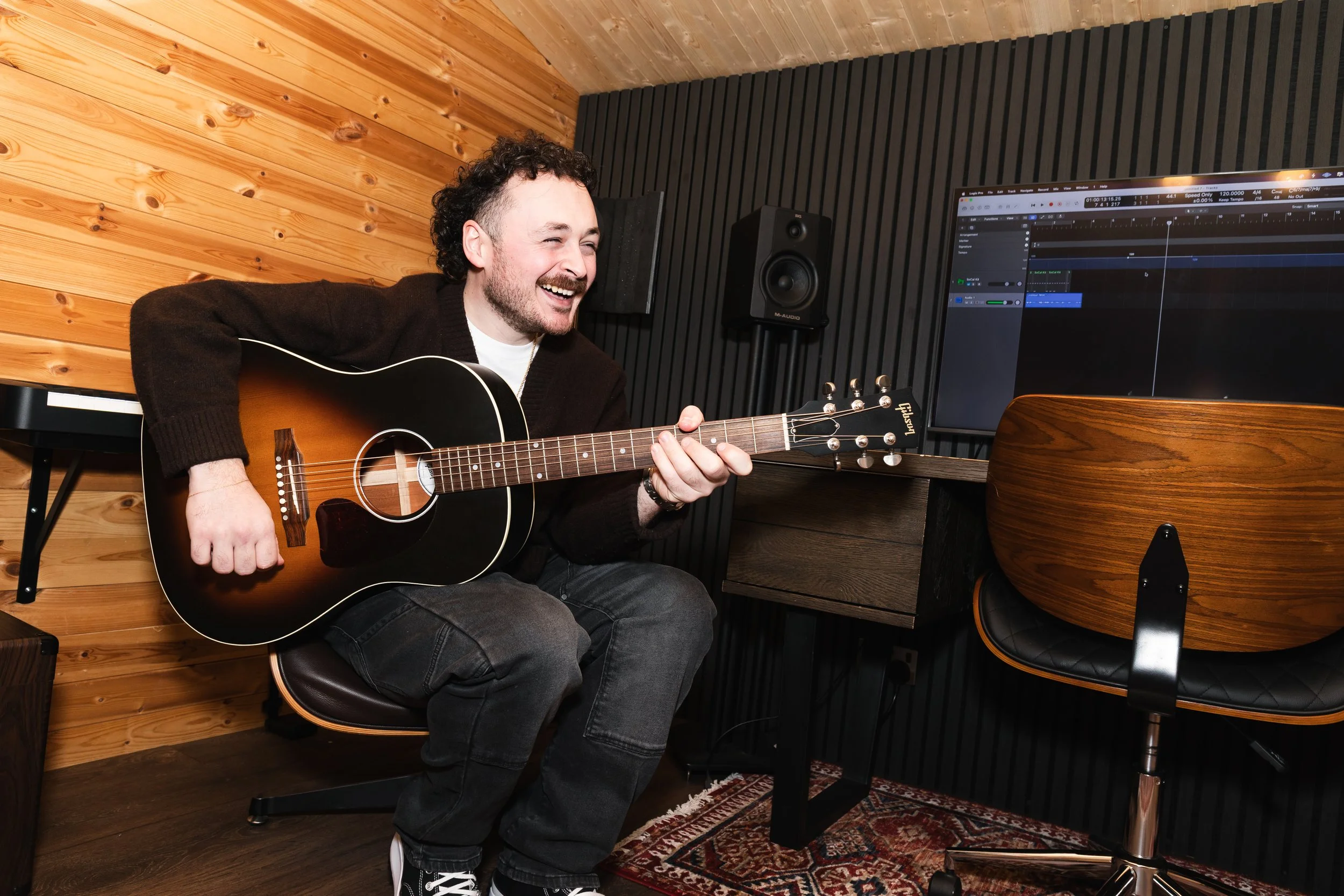 A man smiling while playing an acoustic guitar in a music studio.