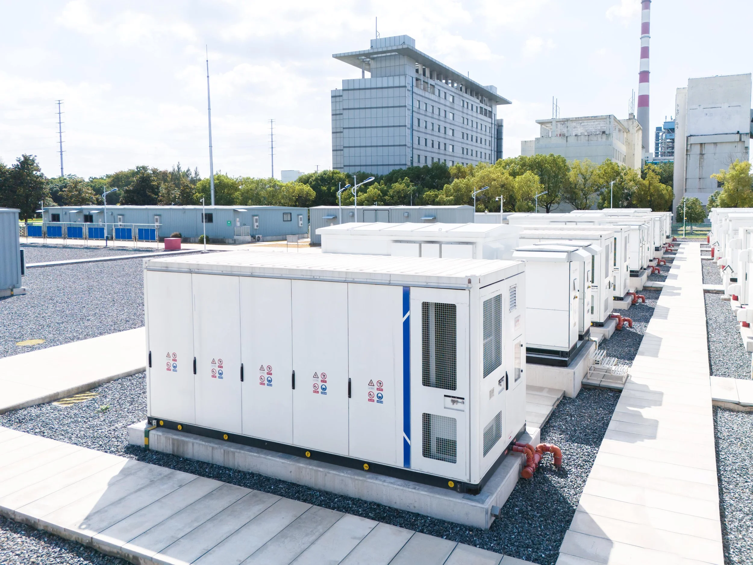Multiple large industrial air conditioning units or generators on rooftops with a cityscape in the background, including modern buildings and a factory with smokestacks.