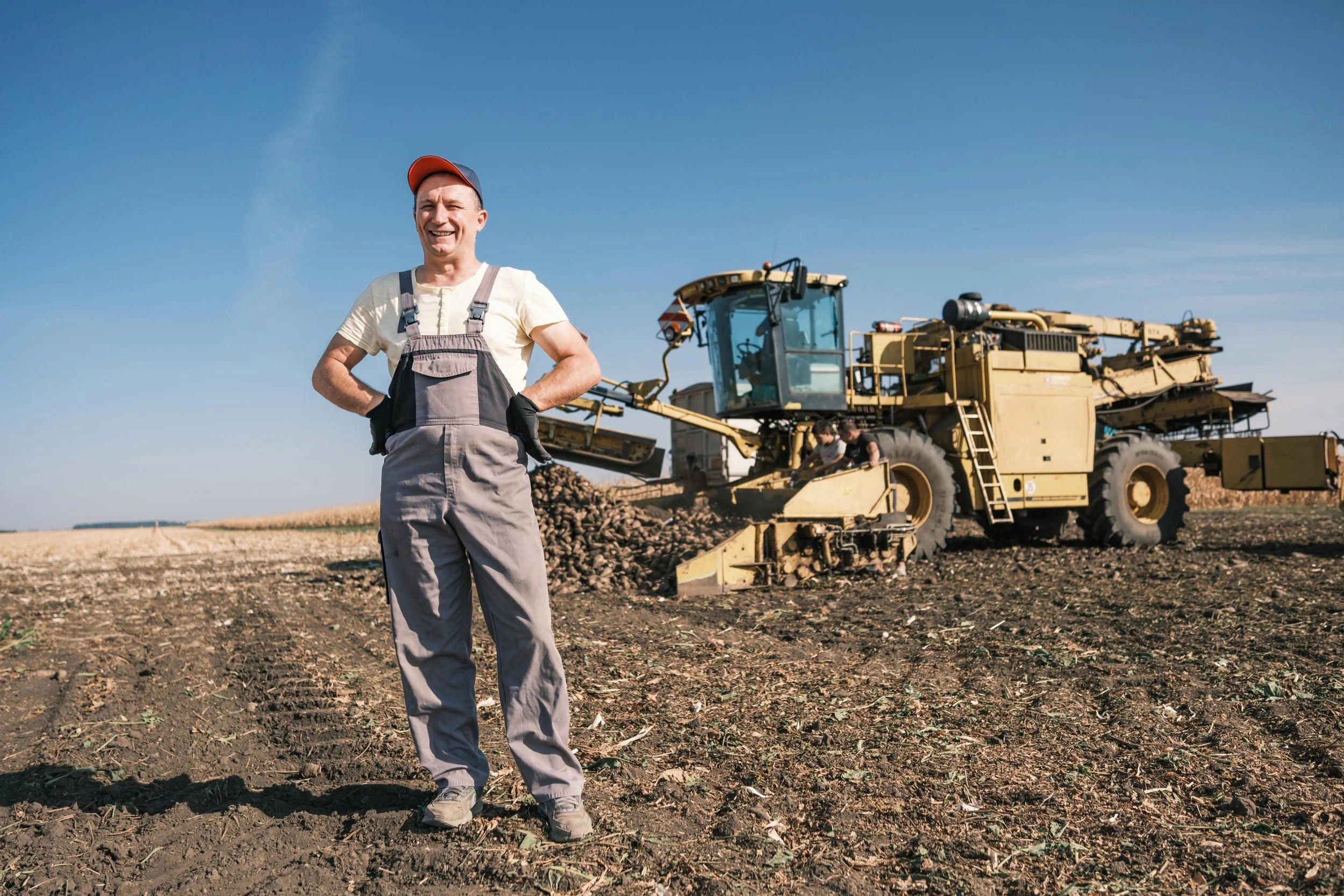 Farmer standing in front of a large yellow tractor working in a field on a clear day.