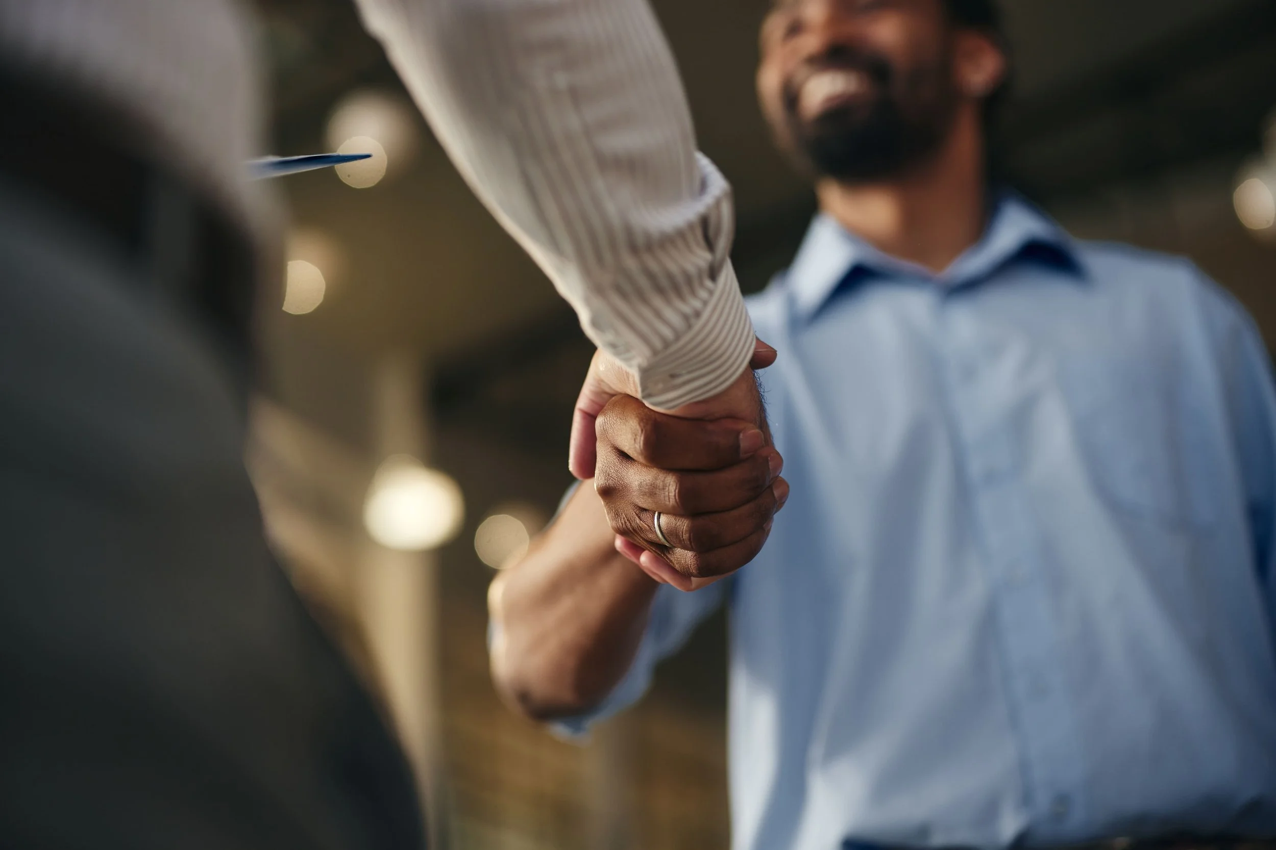 Two men shaking hands, one wearing a light blue shirt, at a professional setting.