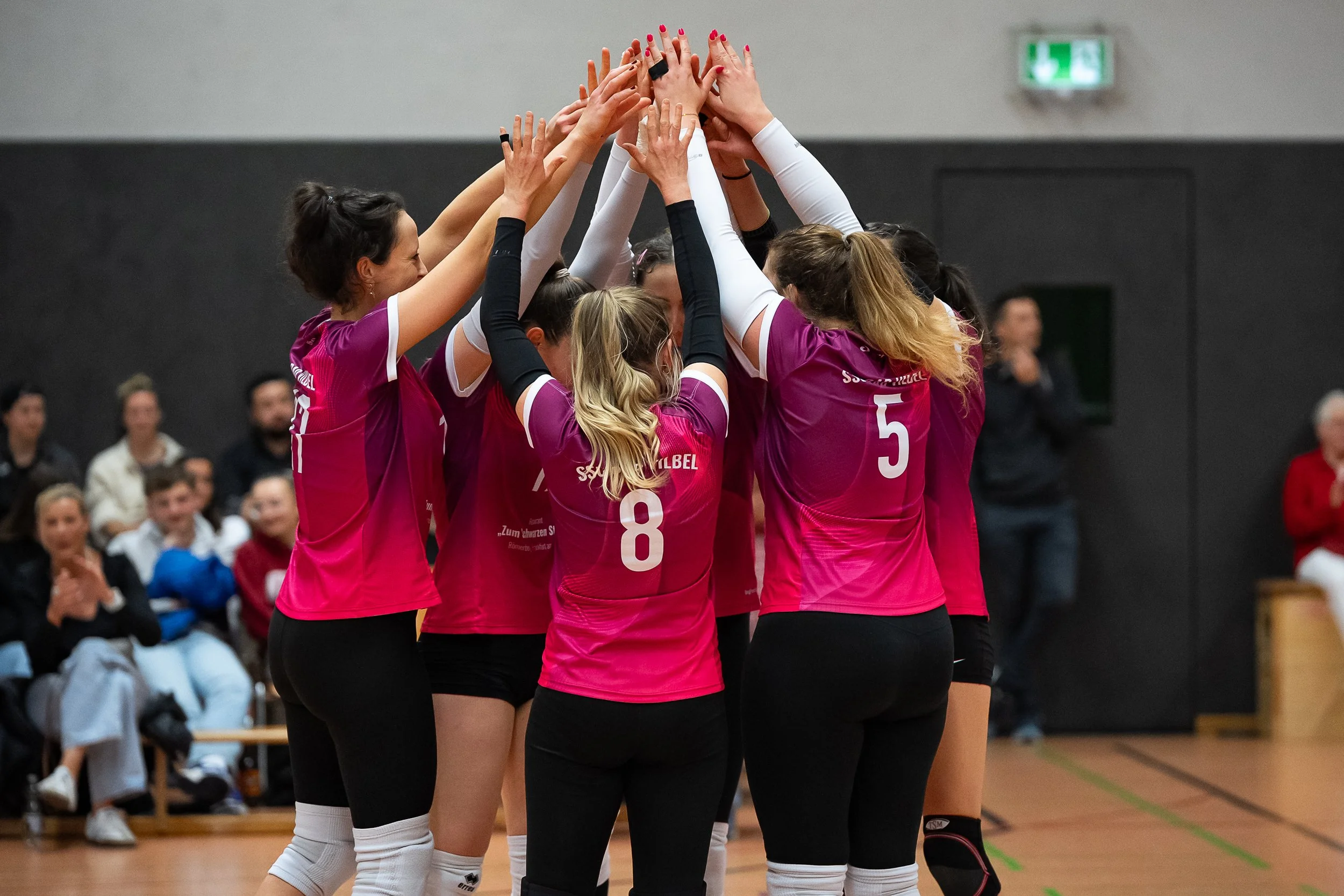 Frauen-Volleyballteam in pink Trikots, die gemeinsam einen Mannschaftsabschluss im Kreis machen.
