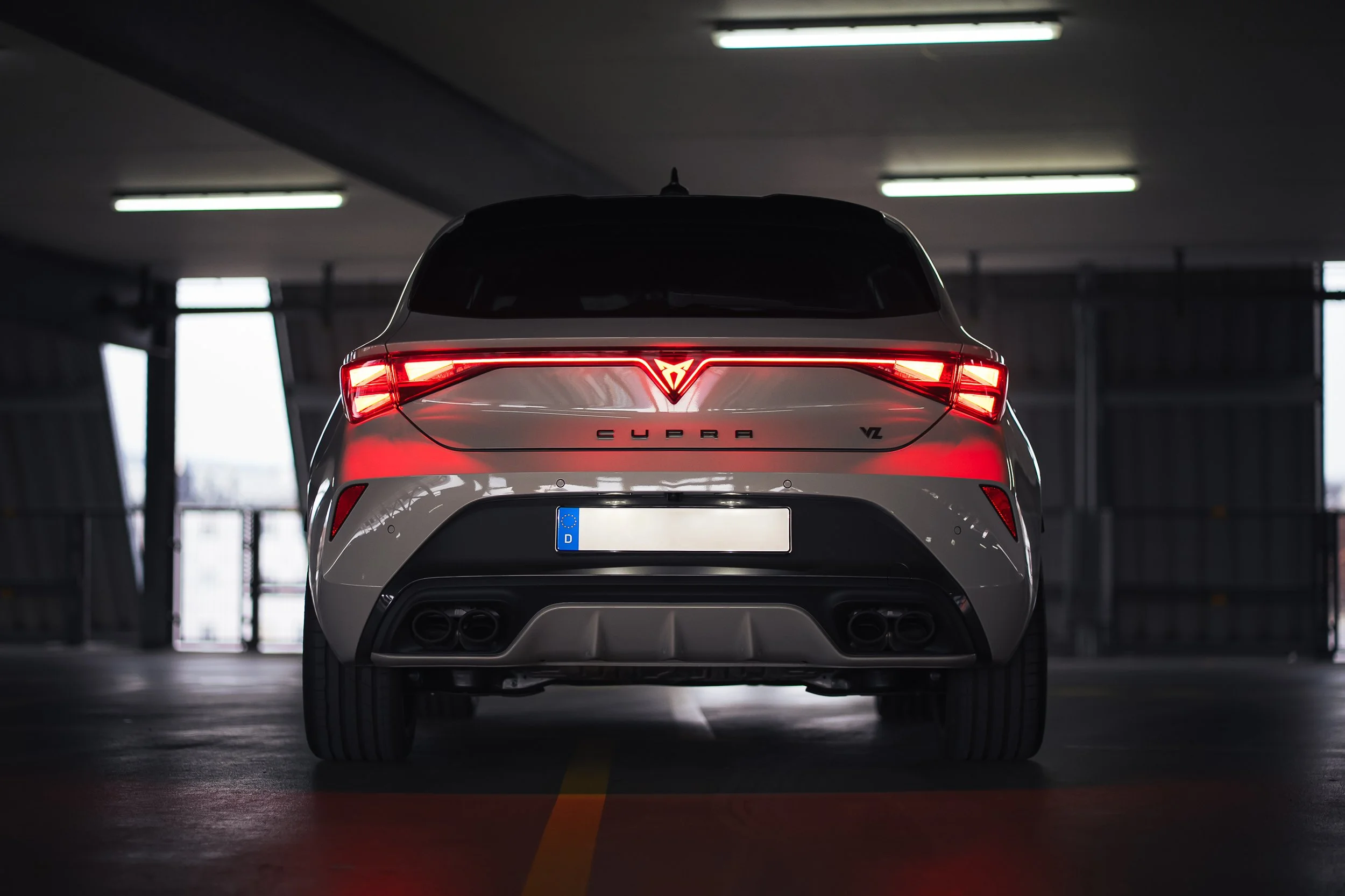 Rückansicht eines Cupra Leon VZ in einer Parkgarage, sichtbar mit leuchtenden roten Rücklichtern, Dachantenne und vier Auspuffrohren.