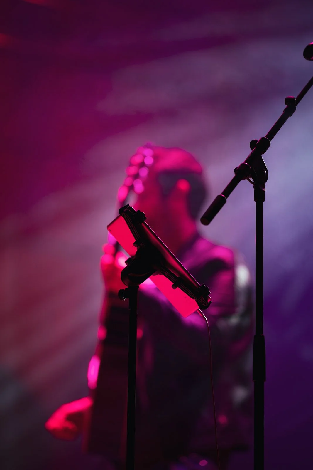 Sänger mit Mikrofon in einem dunklen Raum, beleuchtet mit pinkem Licht, unscharf im Hintergrund.